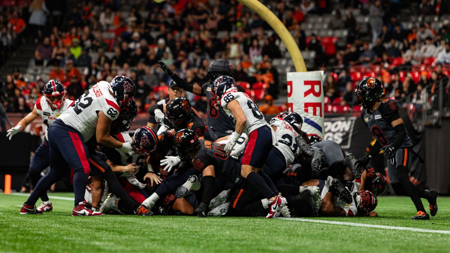 Football players pile up near the goal line during an intense NFL game under stadium lights.