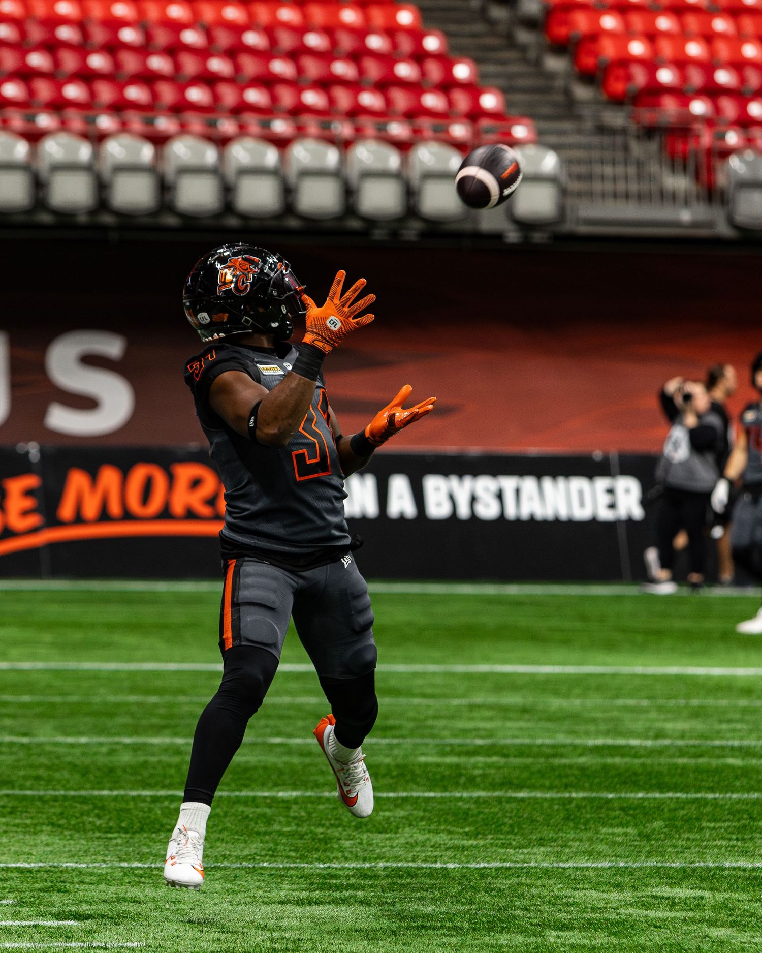BC Lions player in black and orange uniform catches a football on the field at BC Place stadium.