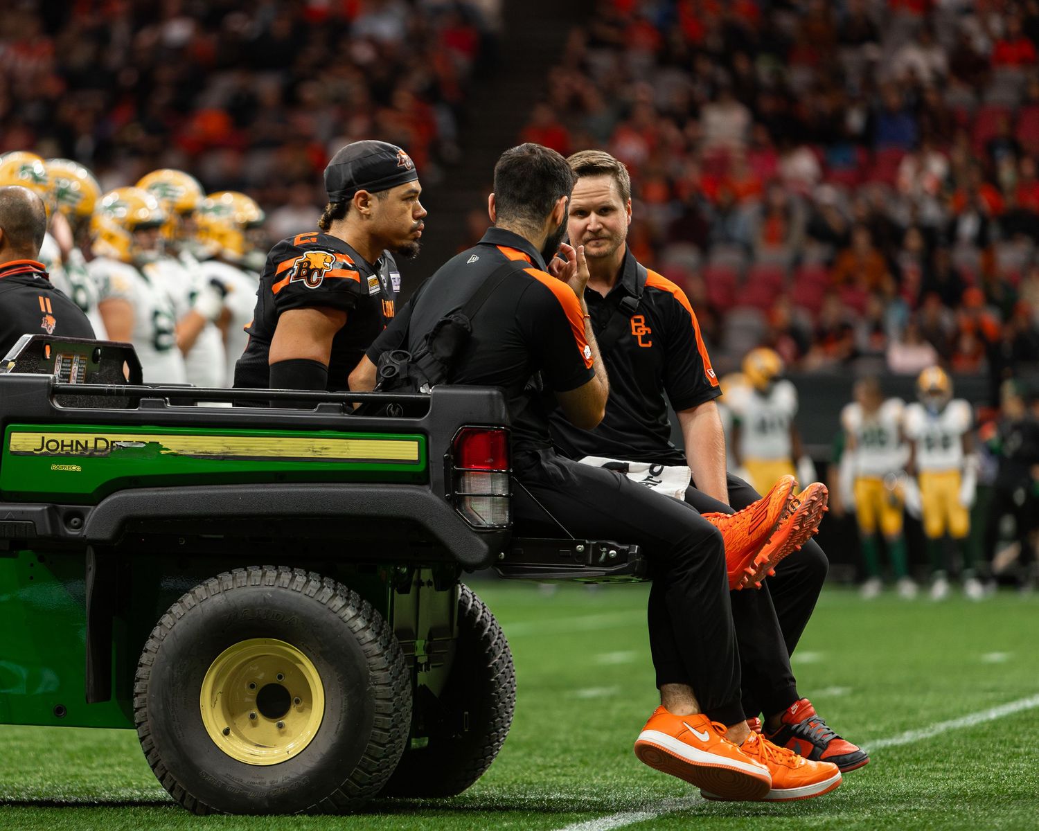Football player being transported on a green cart by medical staff after an injury during a college football game.