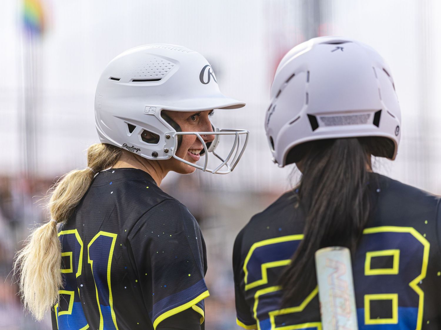 Two softball players in black uniforms and white helmets face each other on the field during a game.