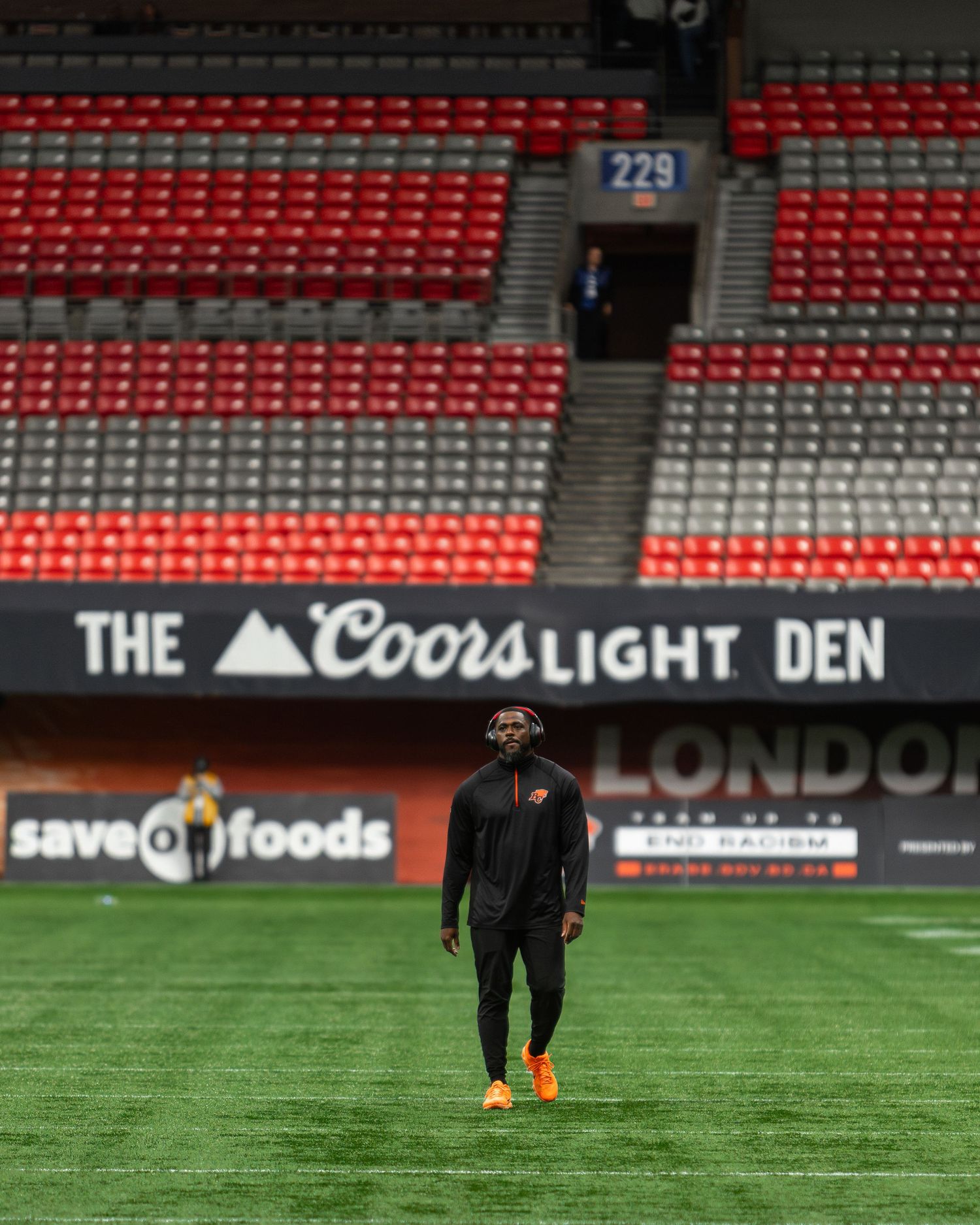 A football player walks on the field at BC Place stadium, home of the BC Lions, with empty red seats behind him.