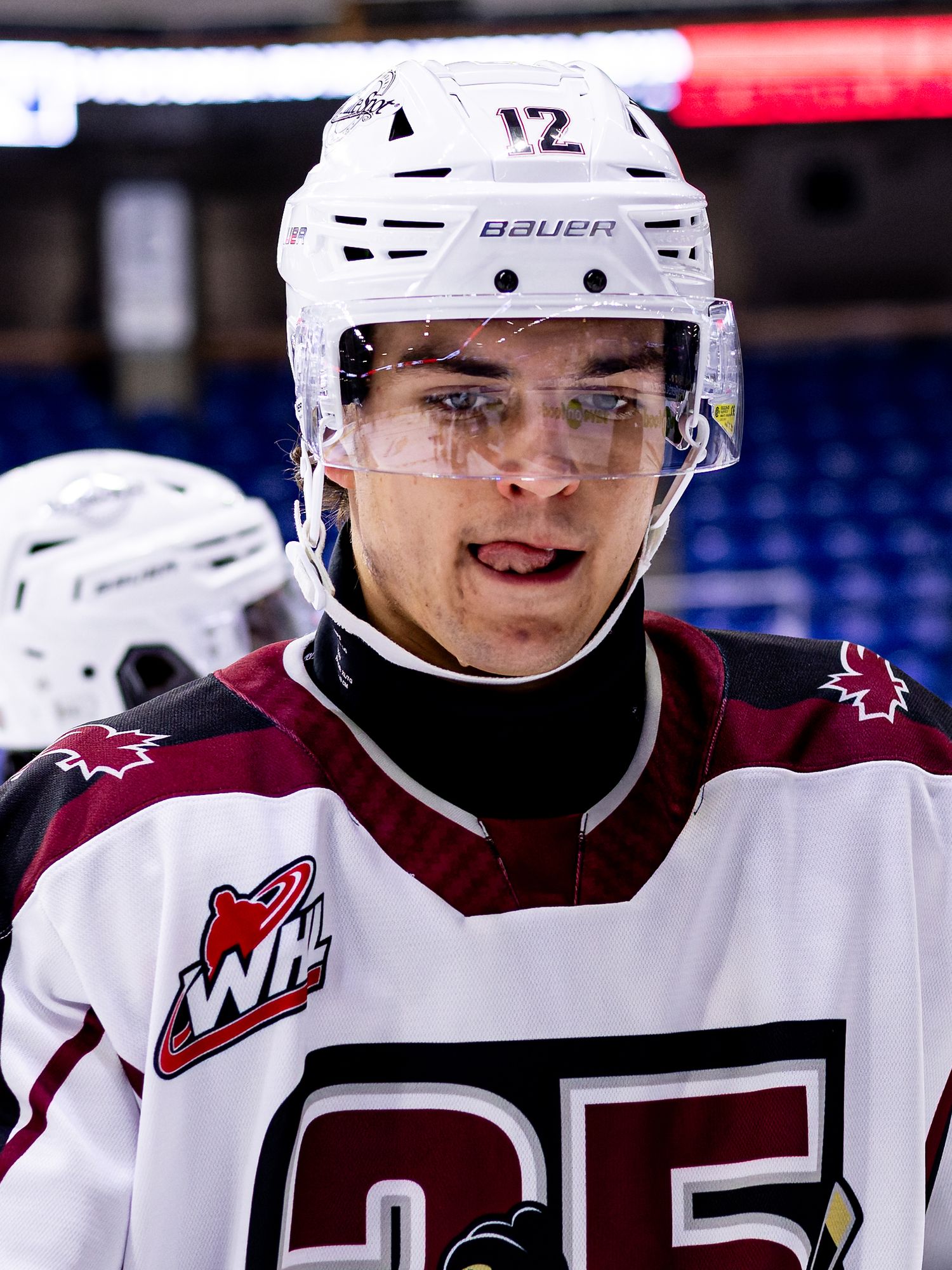 Young WHL hockey player wearing white jersey number 12 and Bauer helmet with visor during game warmups.