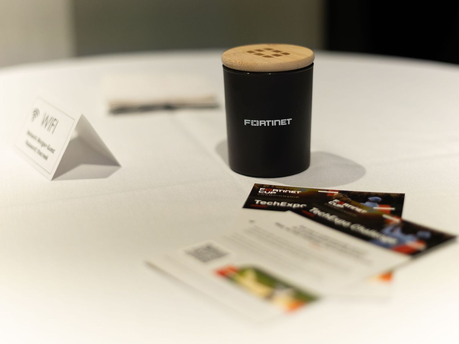 Fortinet branded black canister with cork lid displayed on white table alongside business cards at a tech expo event.