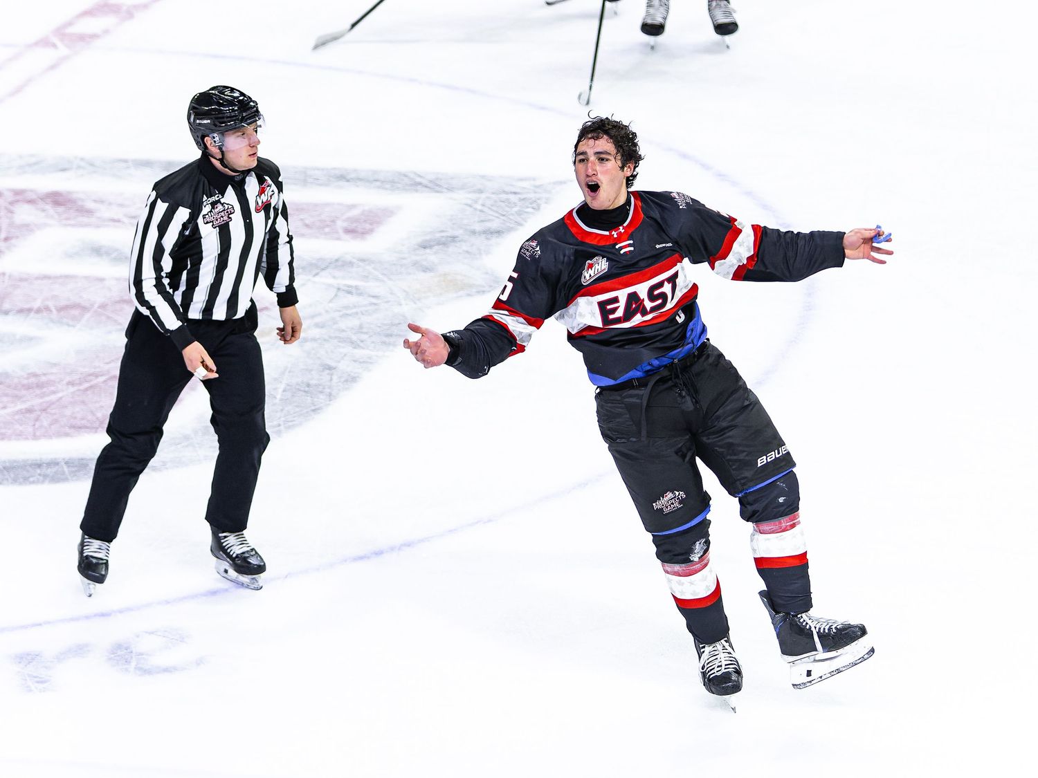 Hockey player in East jersey celebrates on ice rink beside referee during a game.