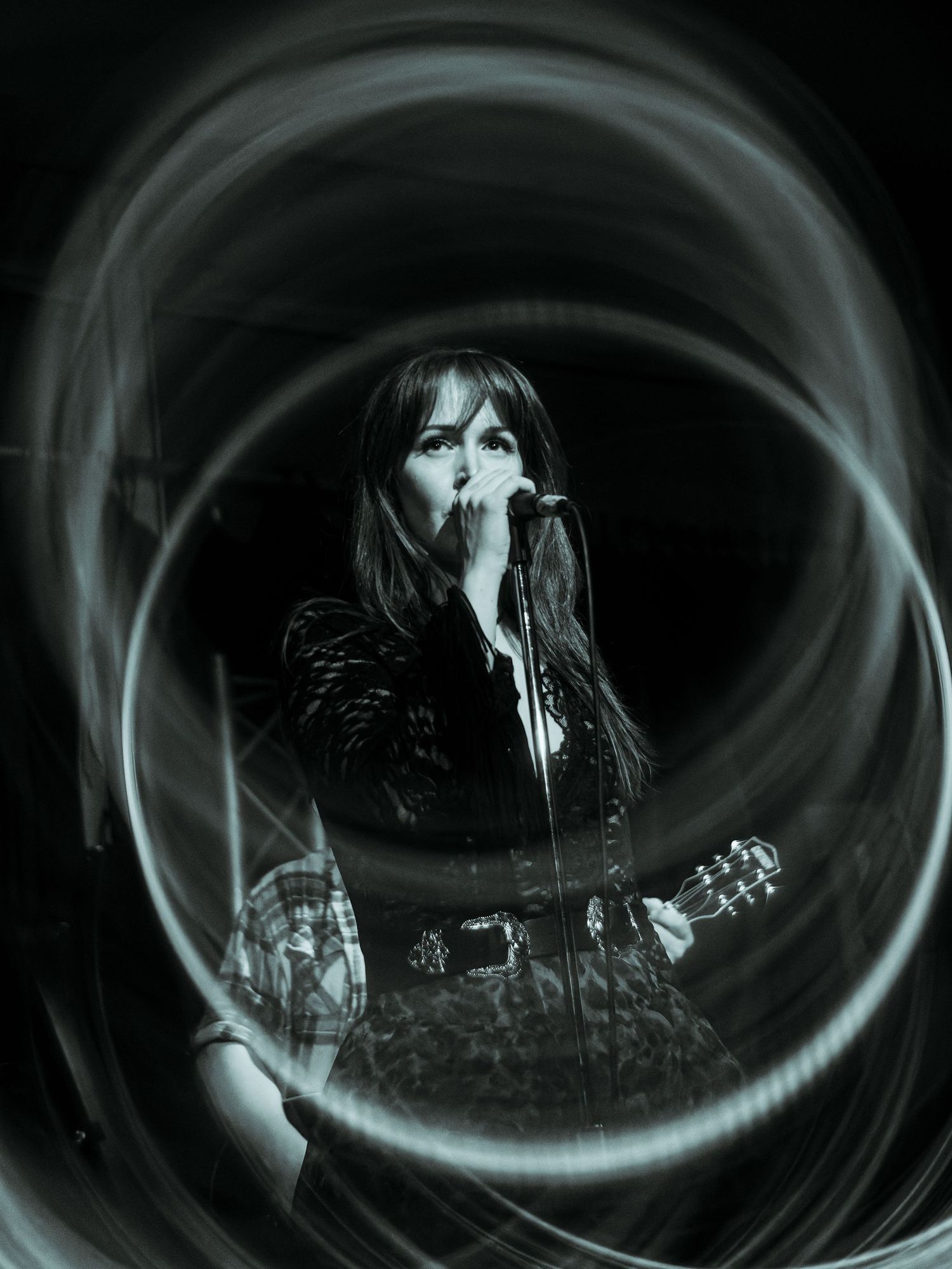 Black and white photo of a female singer performing on stage with a swirling light effect around her.