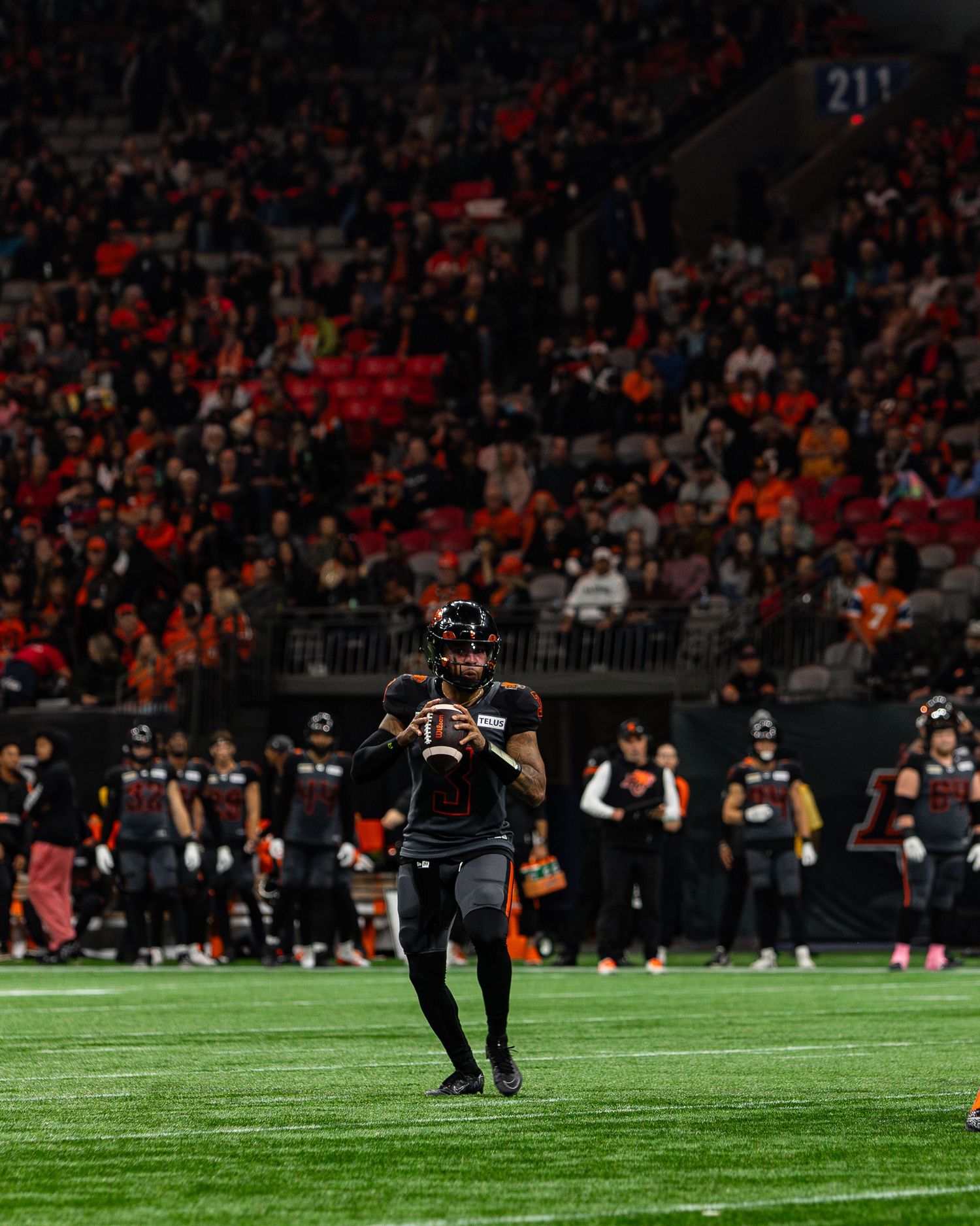 A football player prepares to throw a pass on an indoor field during a night game with packed stadium stands.