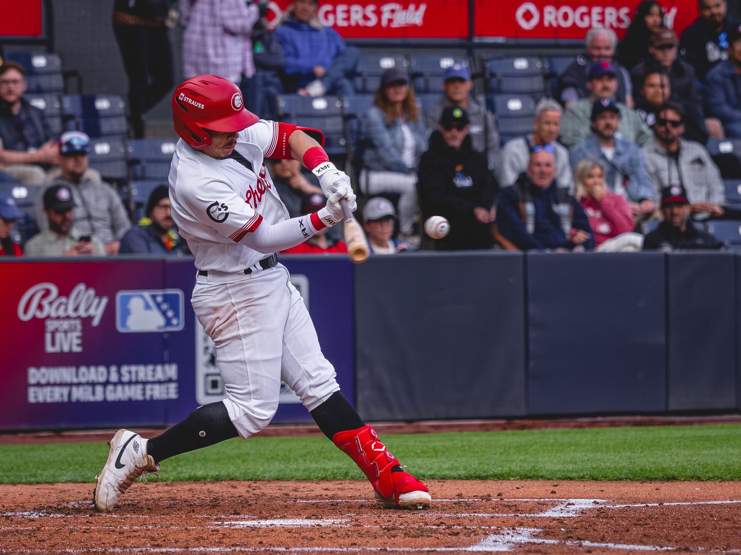 Baseball player in red uniform swinging bat at Rogers Field during a live game.