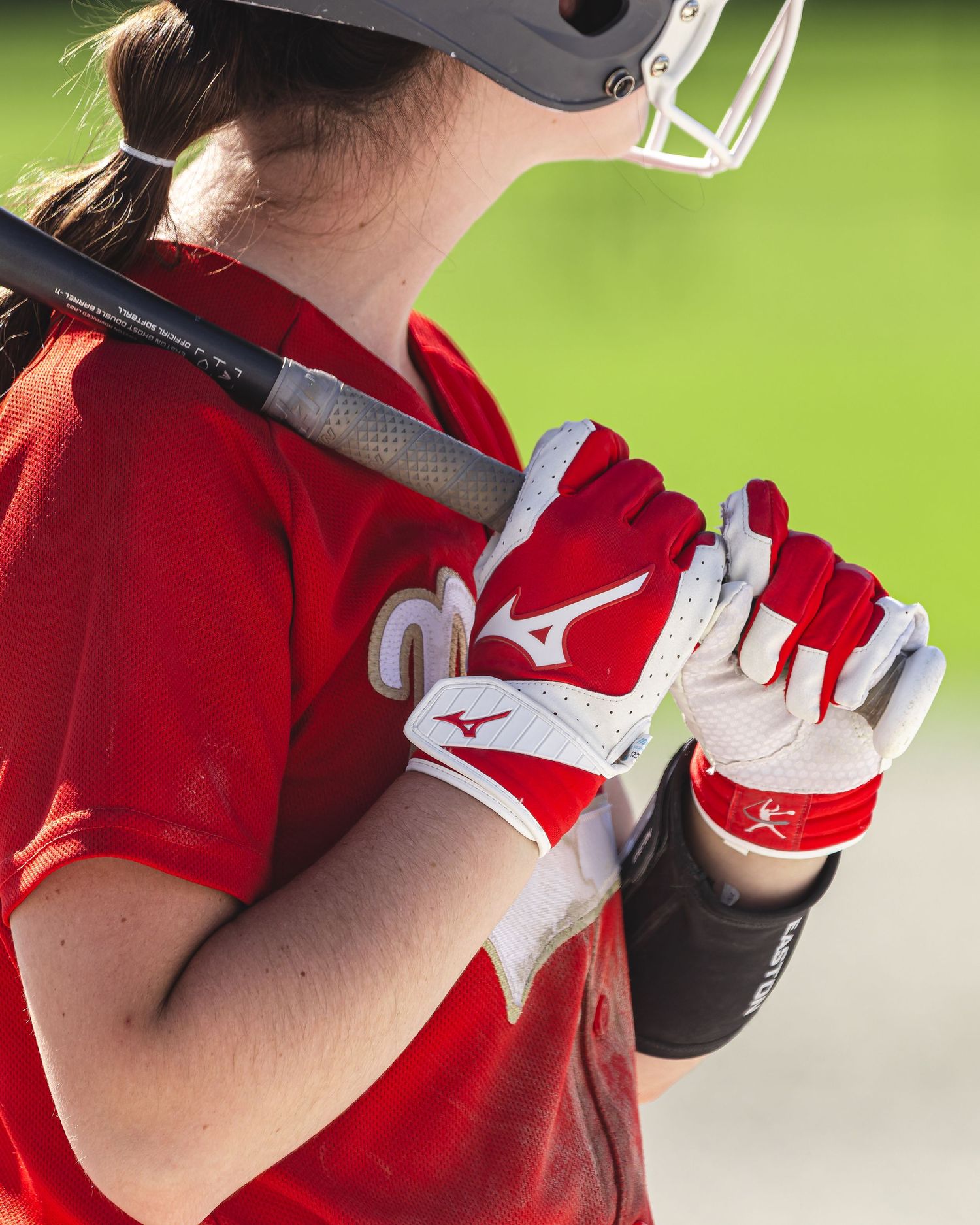 Female softball player in red uniform holding bat with Mizuno gloves.