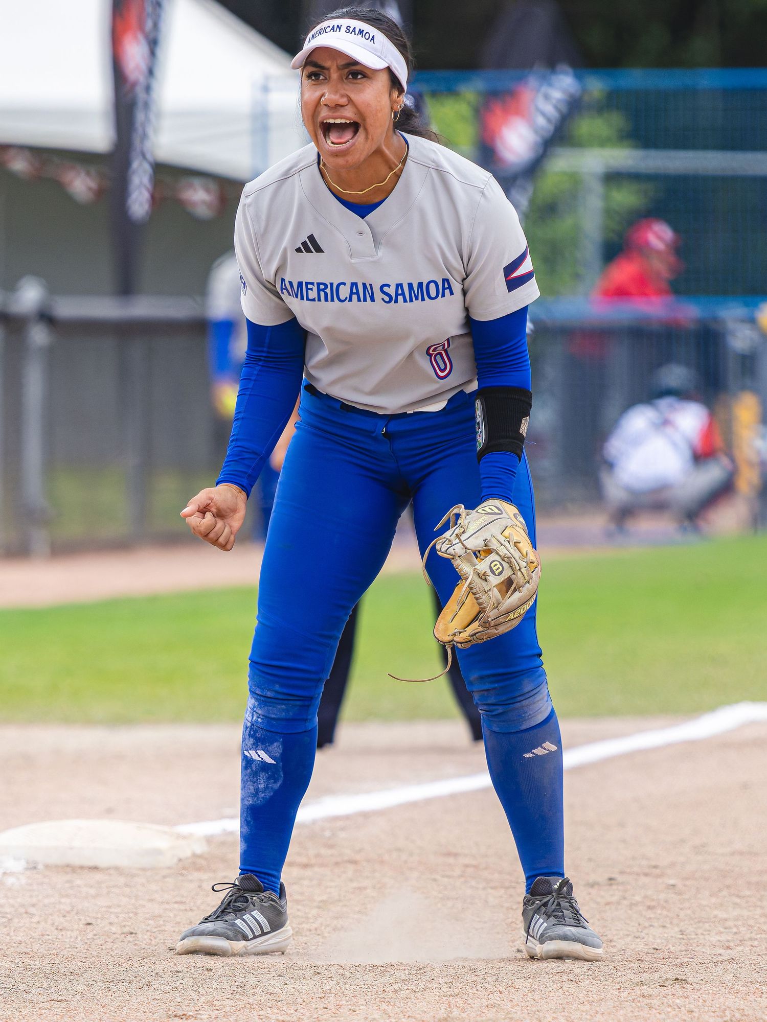 American Samoa softball player celebrates on field wearing blue leggings and gray jersey with glove.