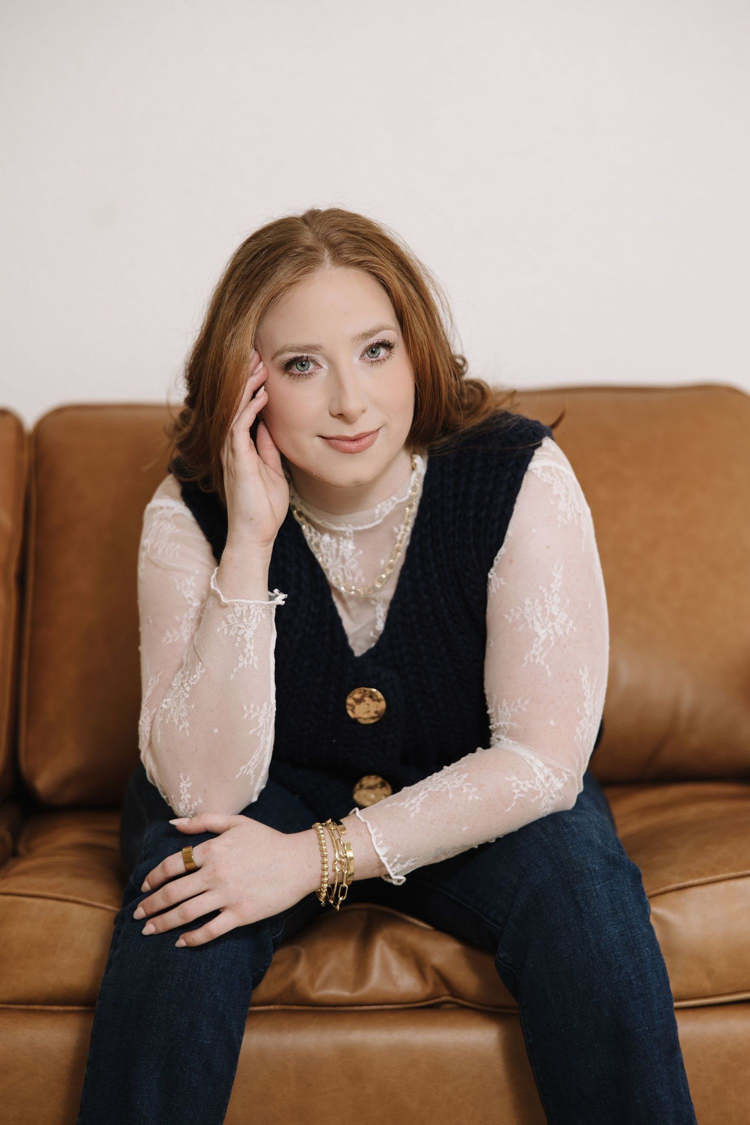 Portrait series on a brown leather couch wearing a black vest and lace blouse.