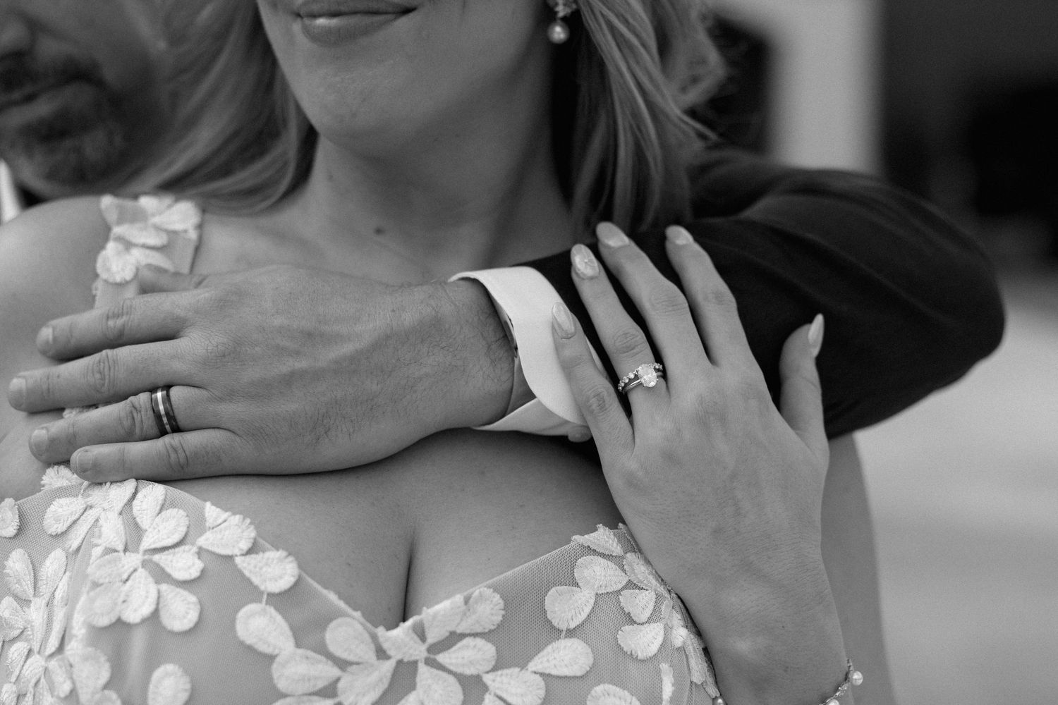 Black and white photo of a couple embracing, showing wedding rings on their hands at a romantic wedding celebration.