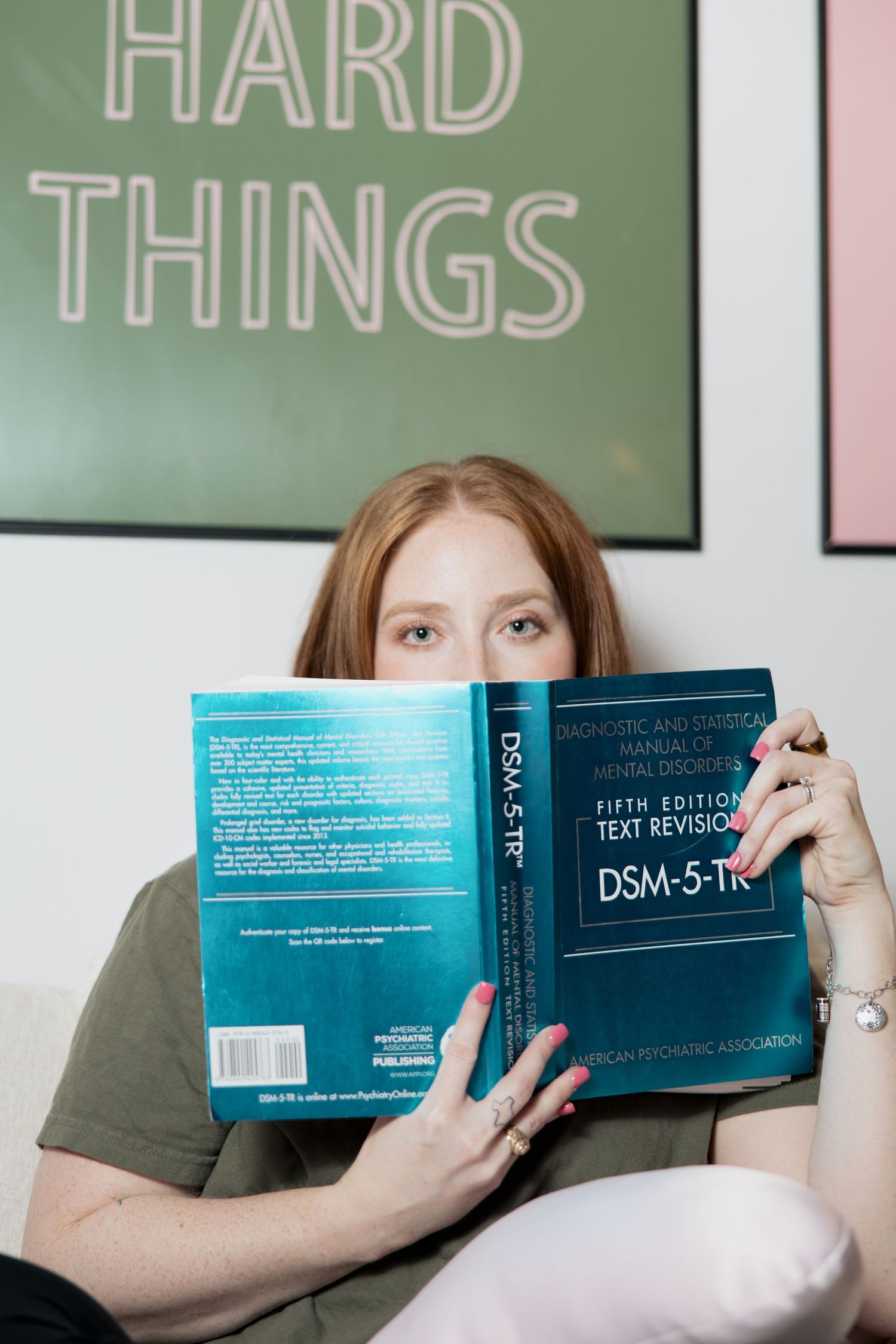 Someone reading the DSM-5 book with a 'Hard Things' sign visible in the background.