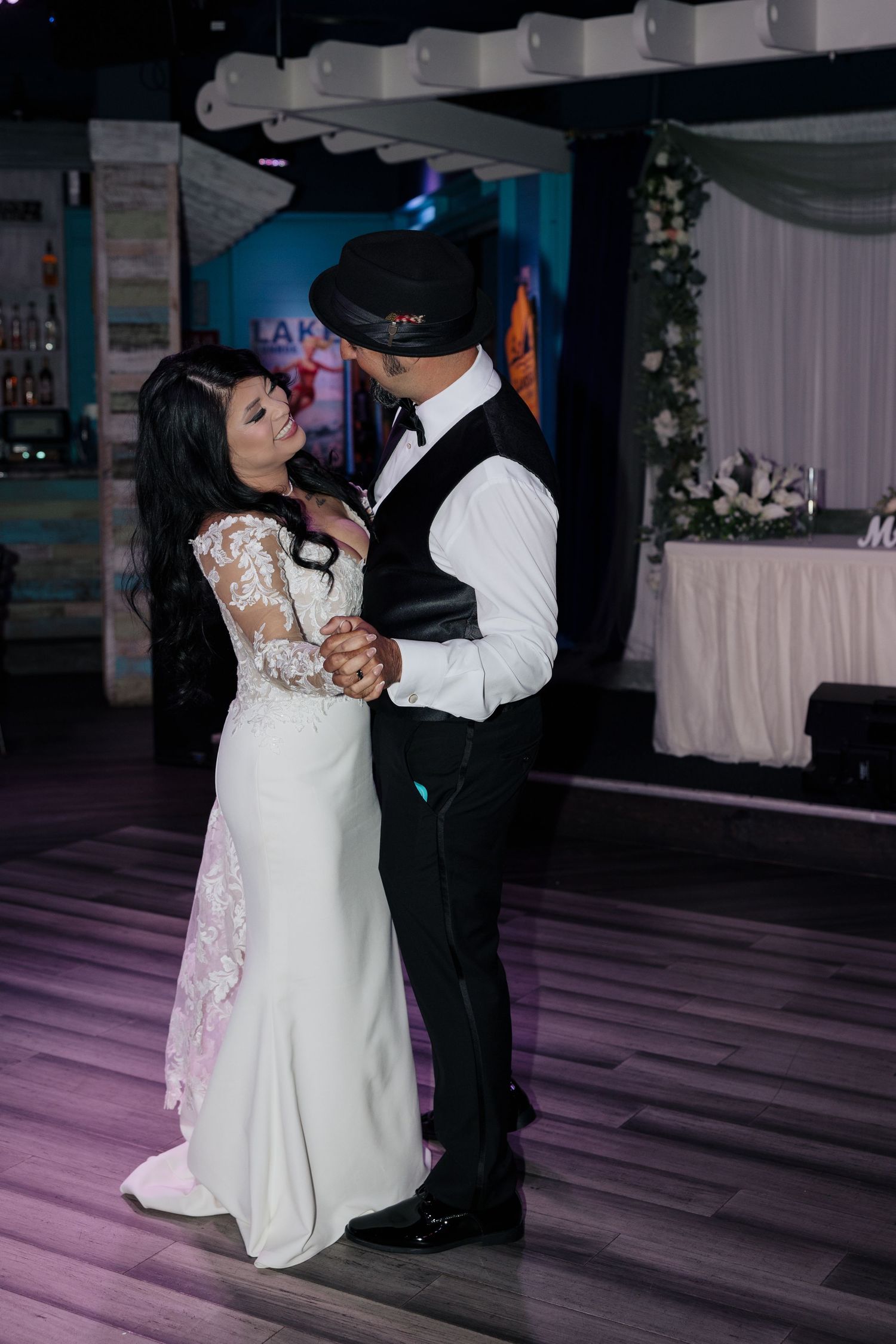 A couple dances together at their wedding reception on a dark wooden dance floor with purple lighting.