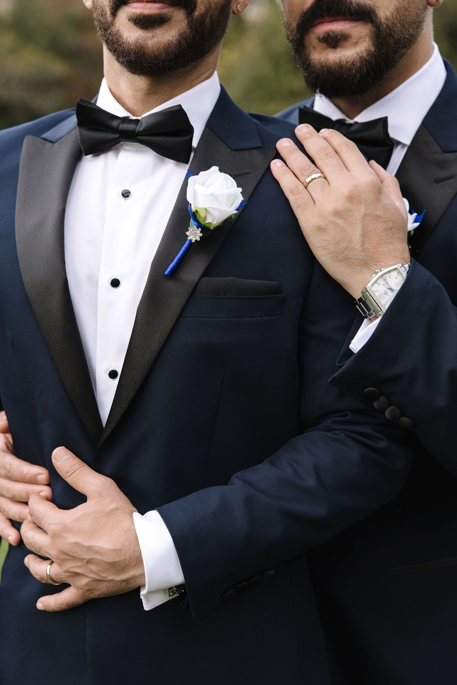 Close-up details of formal black tuxedos with bow ties and white boutonnieres at an elegant wedding celebration.