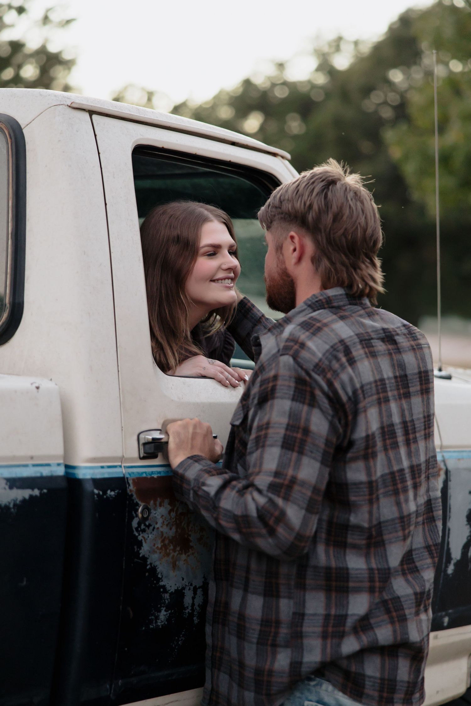 A couple shares an intimate moment beside a white van in a romantic outdoor setting.