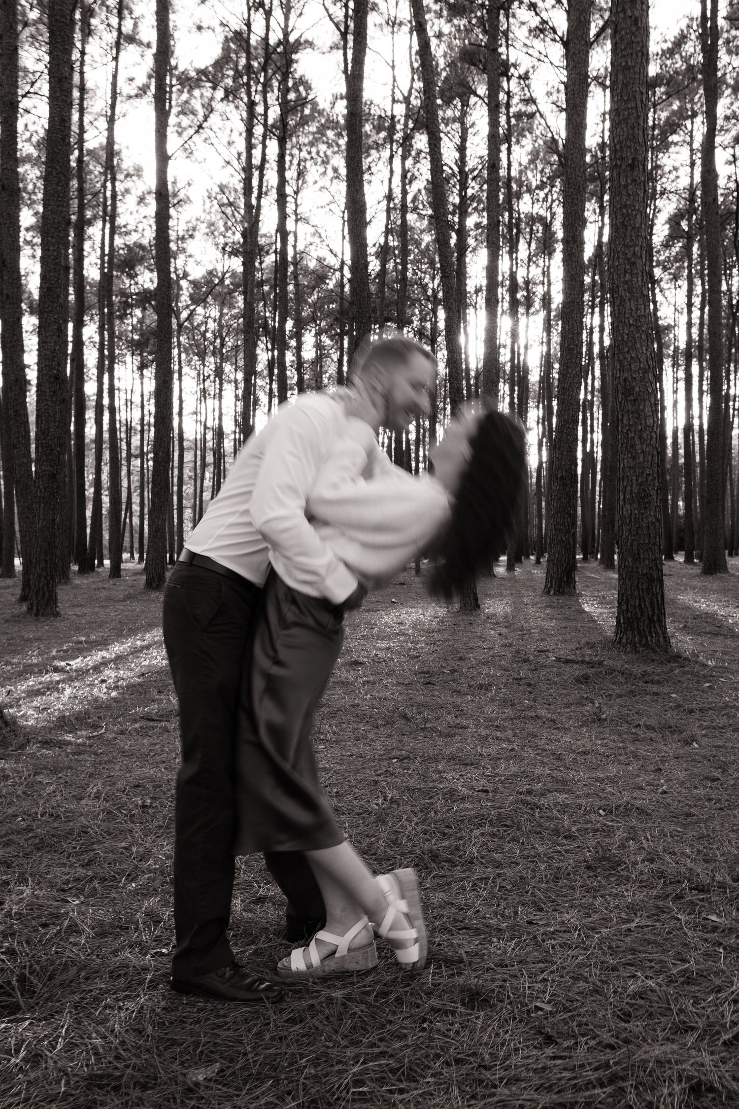 A romantic black and white photograph of a couple dancing in a pine forest.