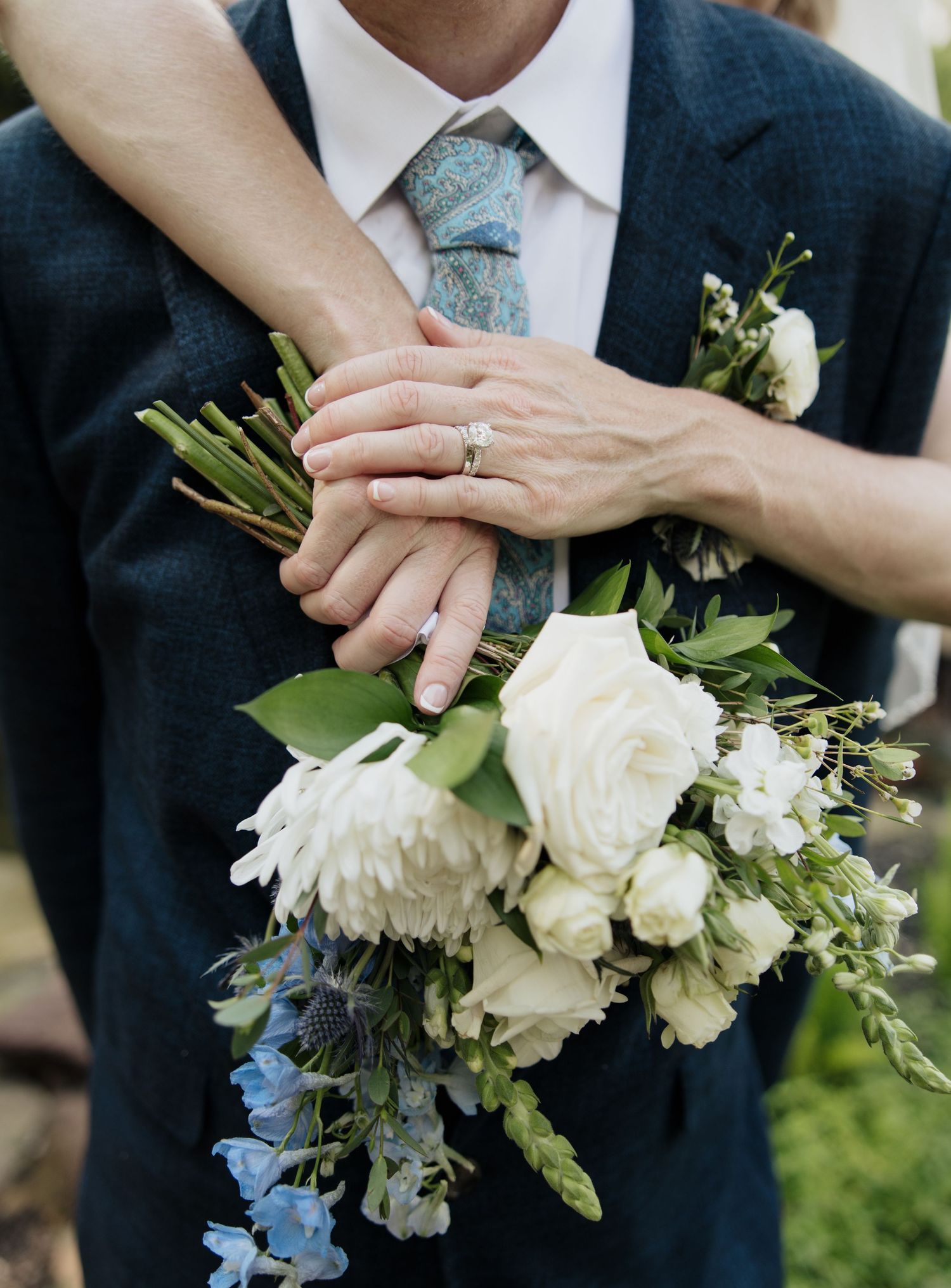 Close-up of white and blue floral wedding bouquet against navy suit.