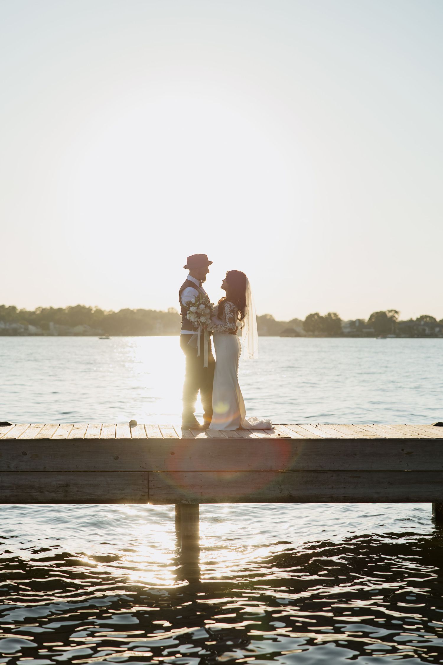 Silhouettes of a couple sitting on a wooden dock at sunset by a tranquil lake.