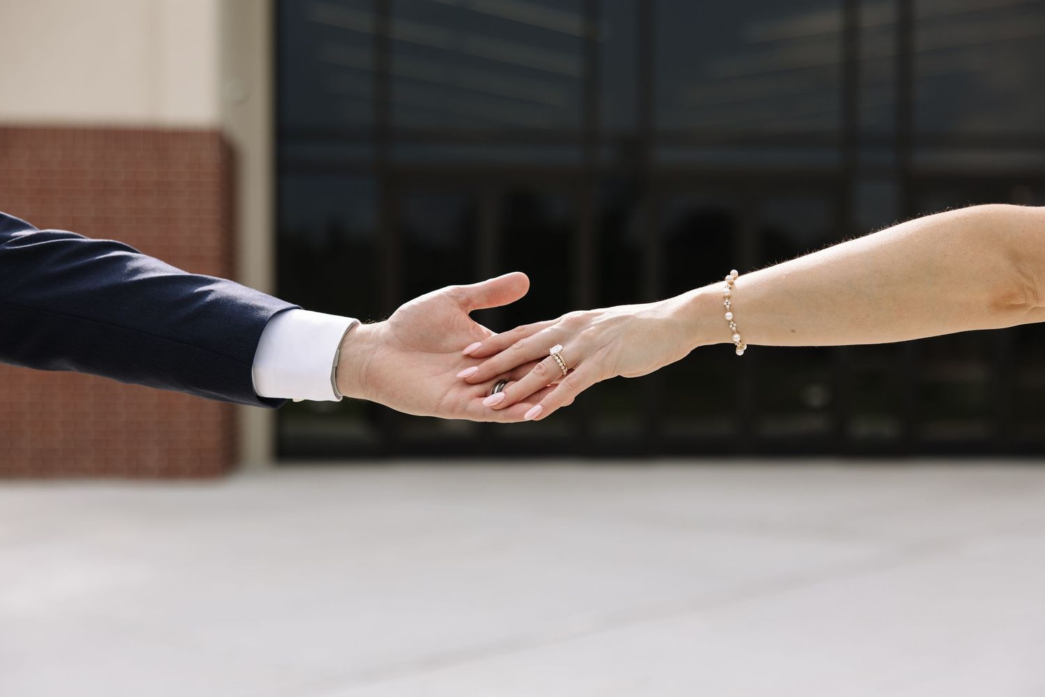 Two people reaching out to shake hands in a professional setting, one wearing a suit and the other a delicate bracelet.