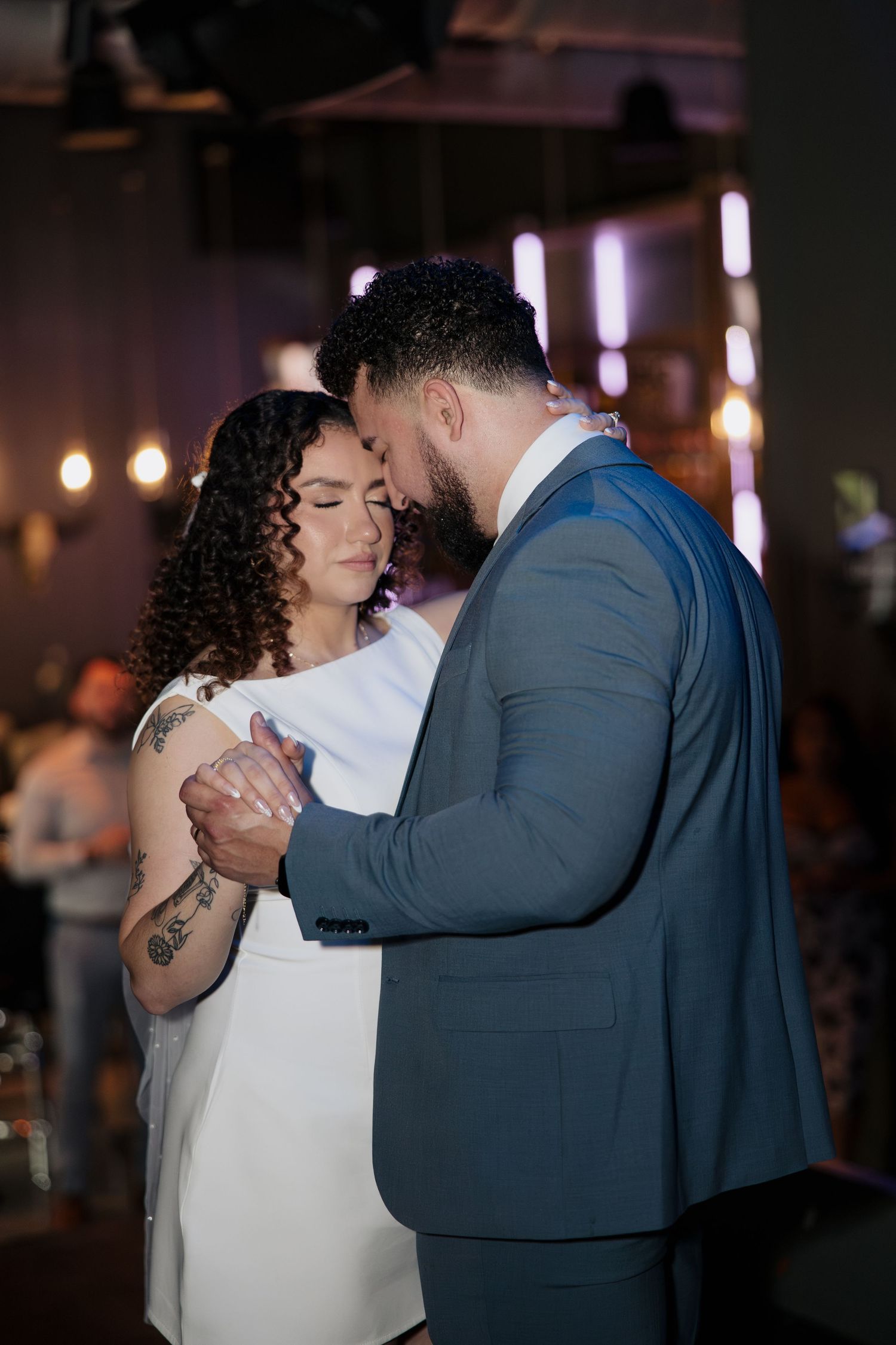 A couple sharing an intimate dance moment in formal attire at a dimly lit venue.