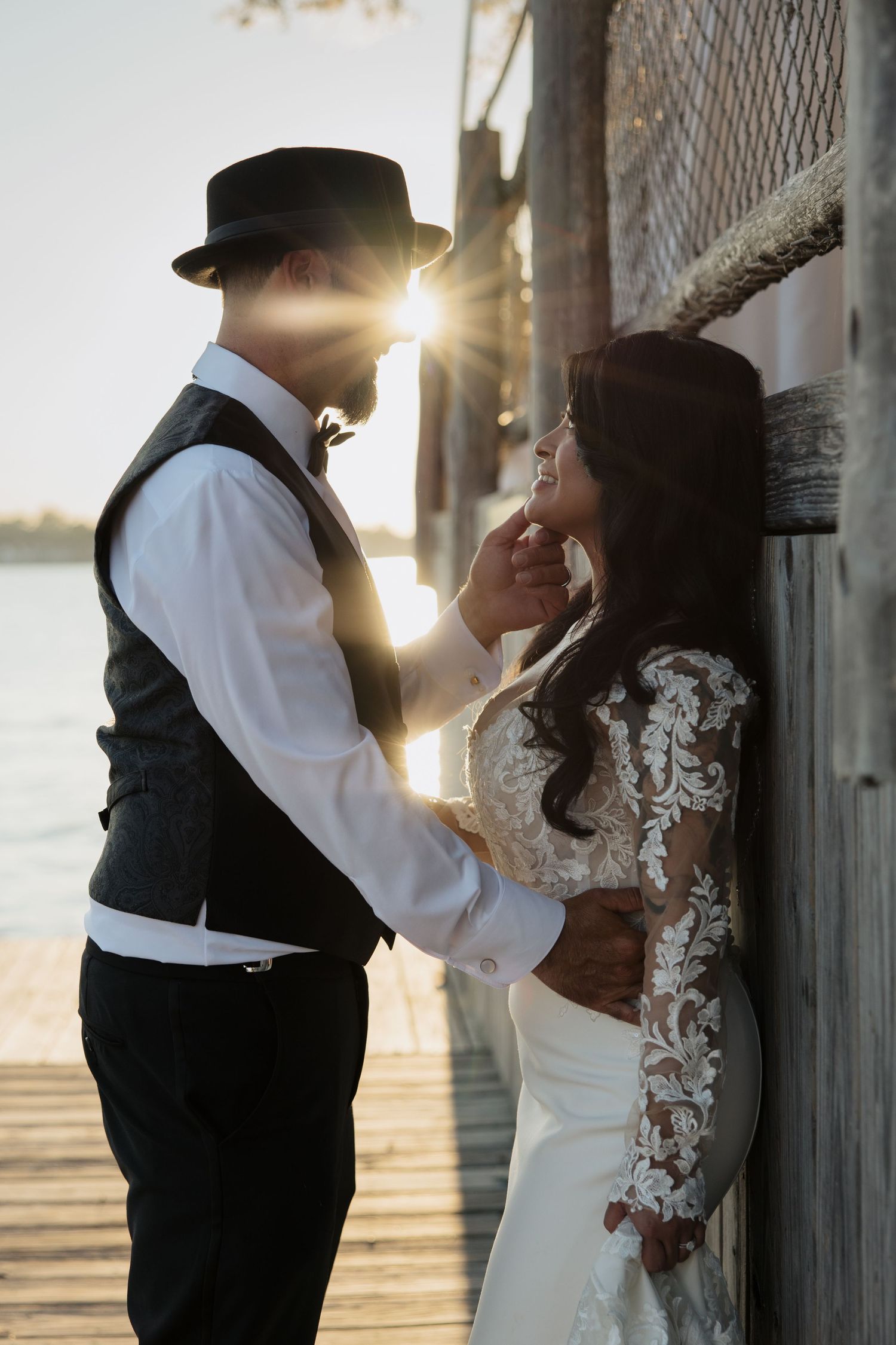 A romantic sunset wedding photoshoot shows a couple embracing against a rustic backdrop with golden sunlight.