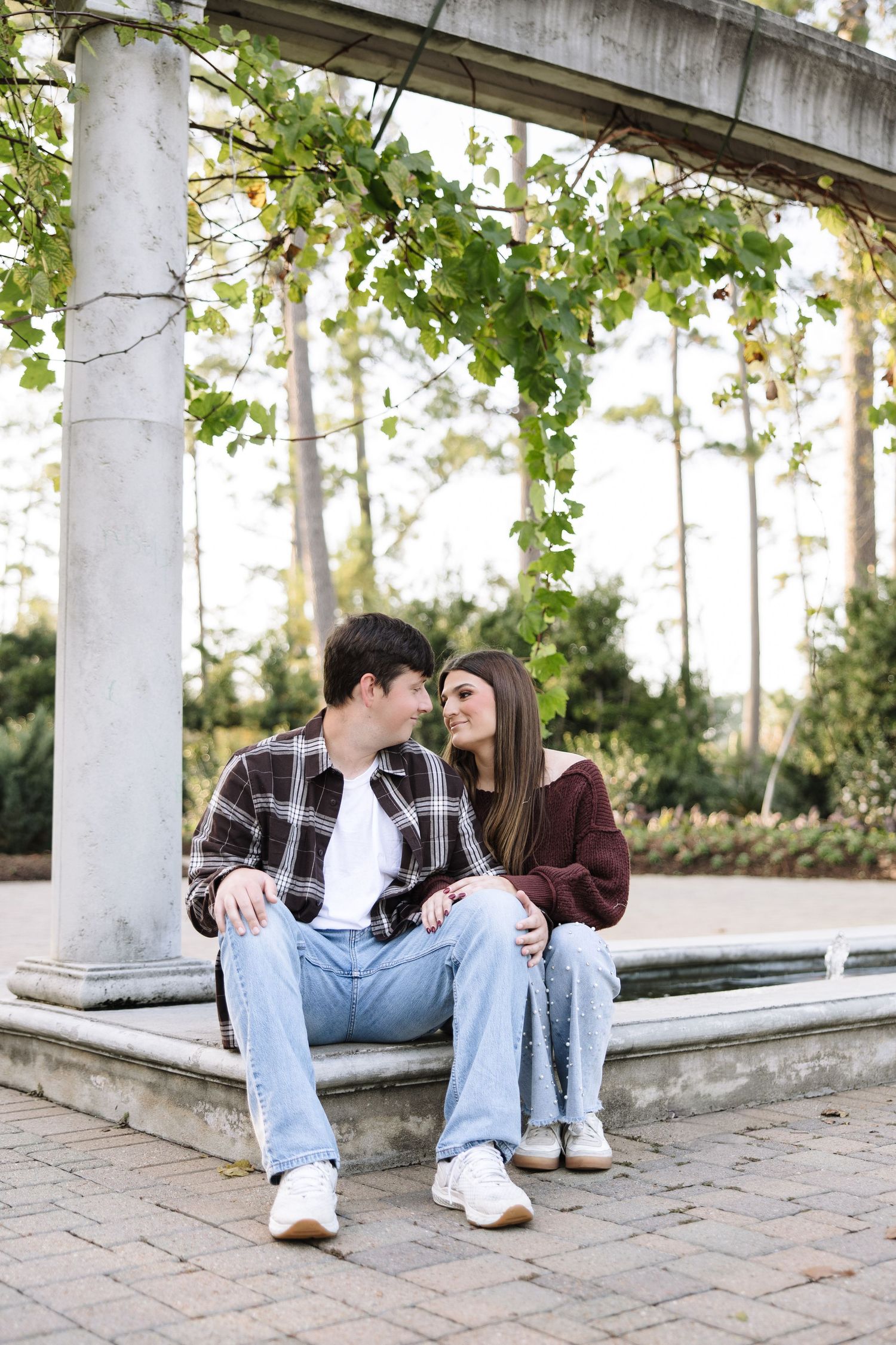 Romantic couple photos taken under a white pergola surrounded by green foliage.