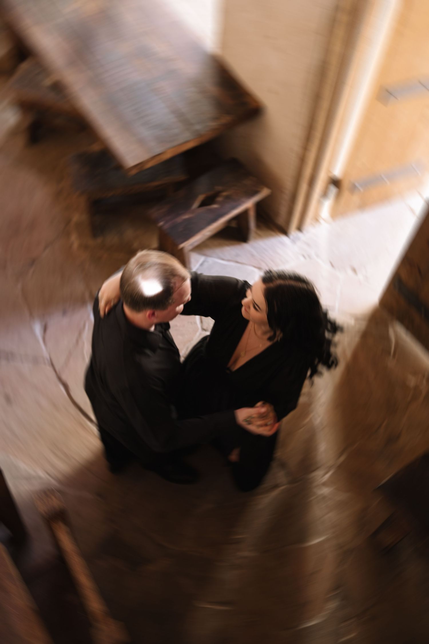 Aerial view of couple in black embracing on rustic wooden floor, sharing an intimate moment.