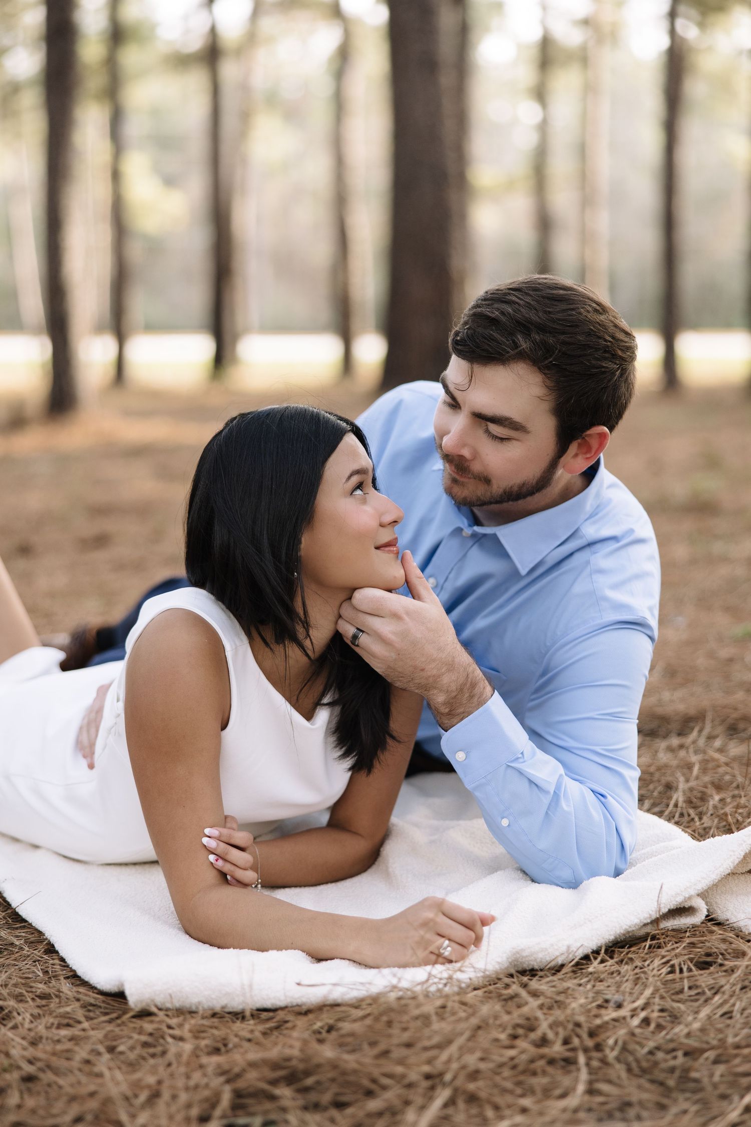 Romantic couple lying on blanket in forest setting during engagement photo session.