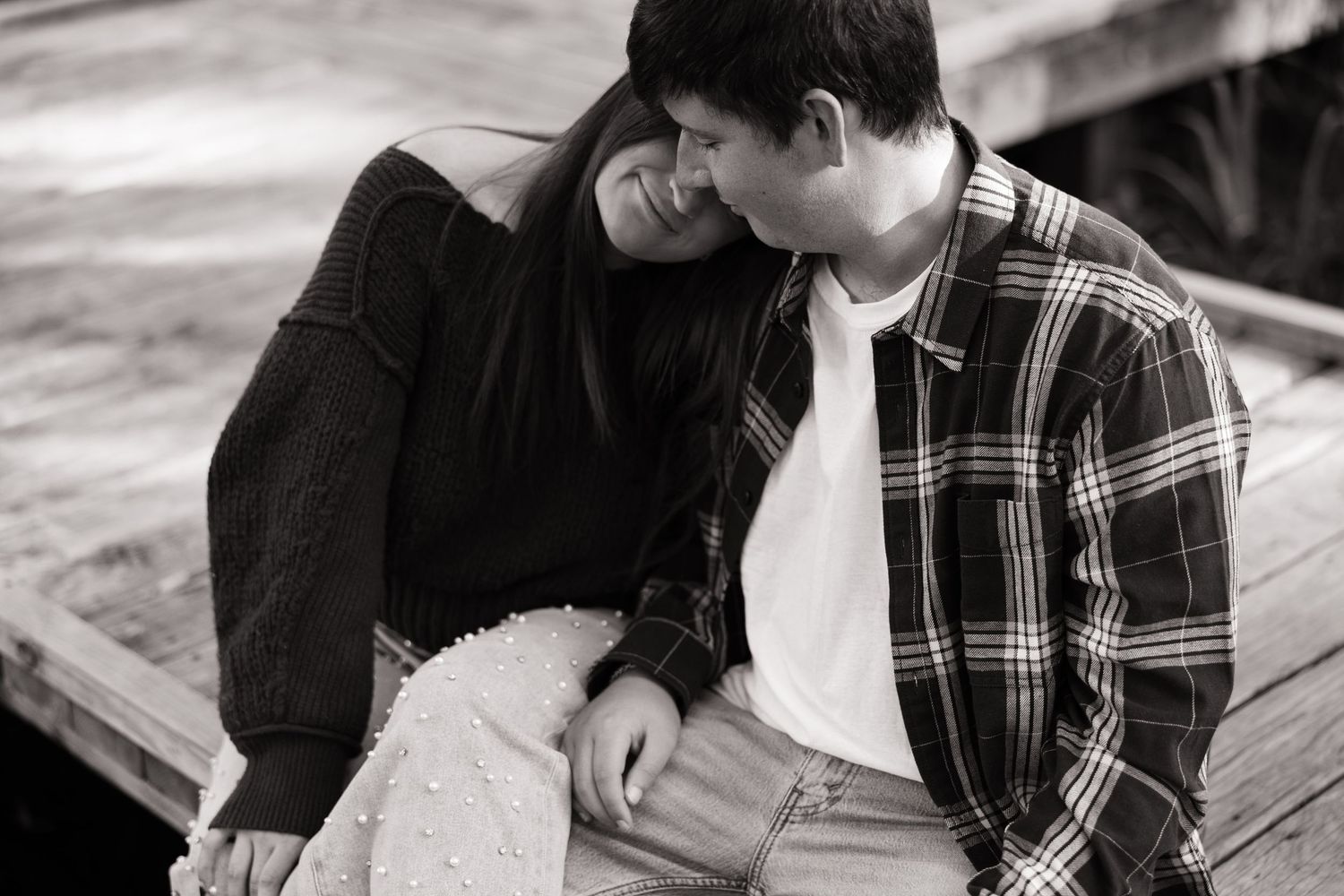 Black and white photo of a couple in casual wear sitting close together and sharing an intimate moment on wooden steps.