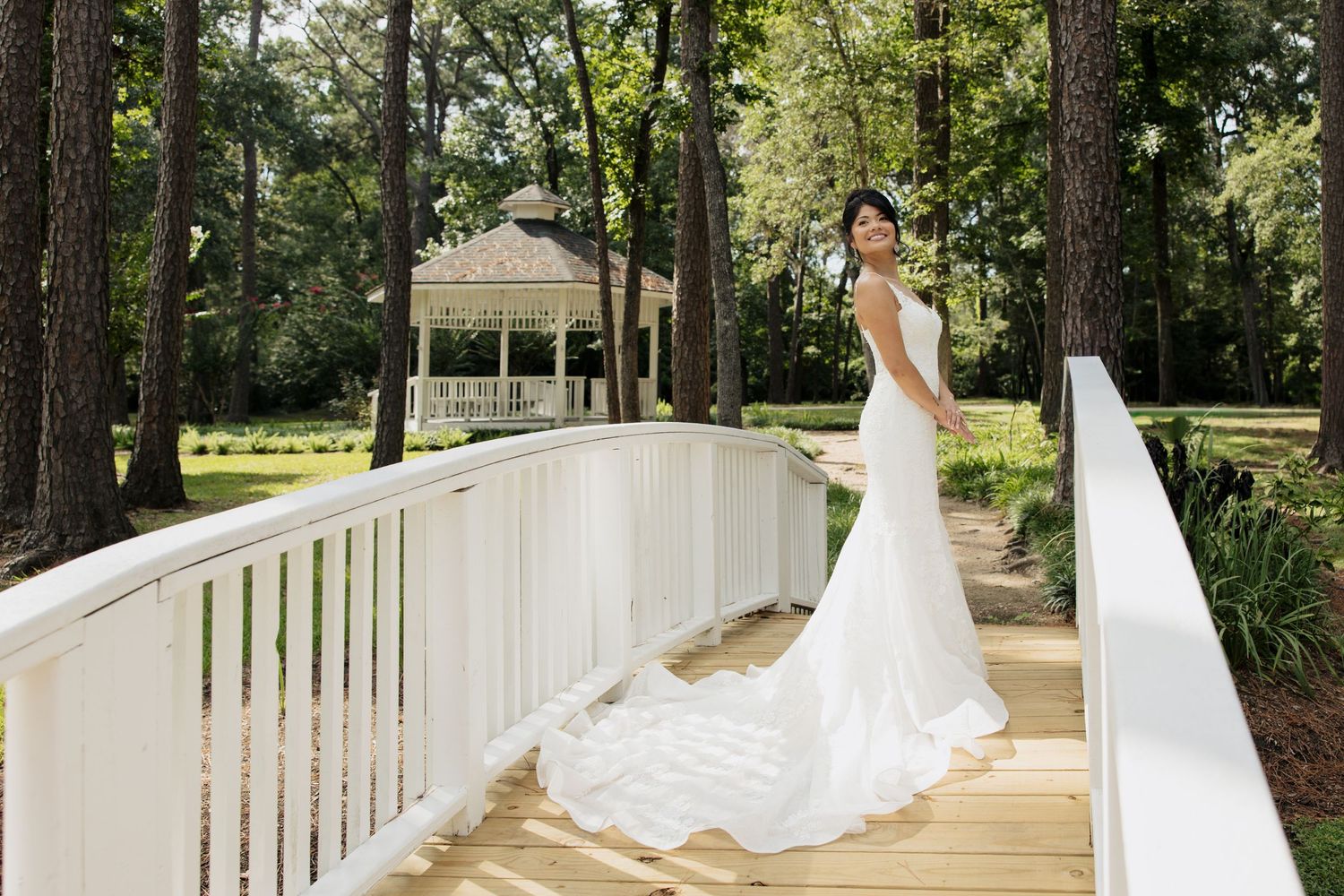 Elegant bridal portraits taken in front of a white gazebo with trailing wedding dress in natural setting.