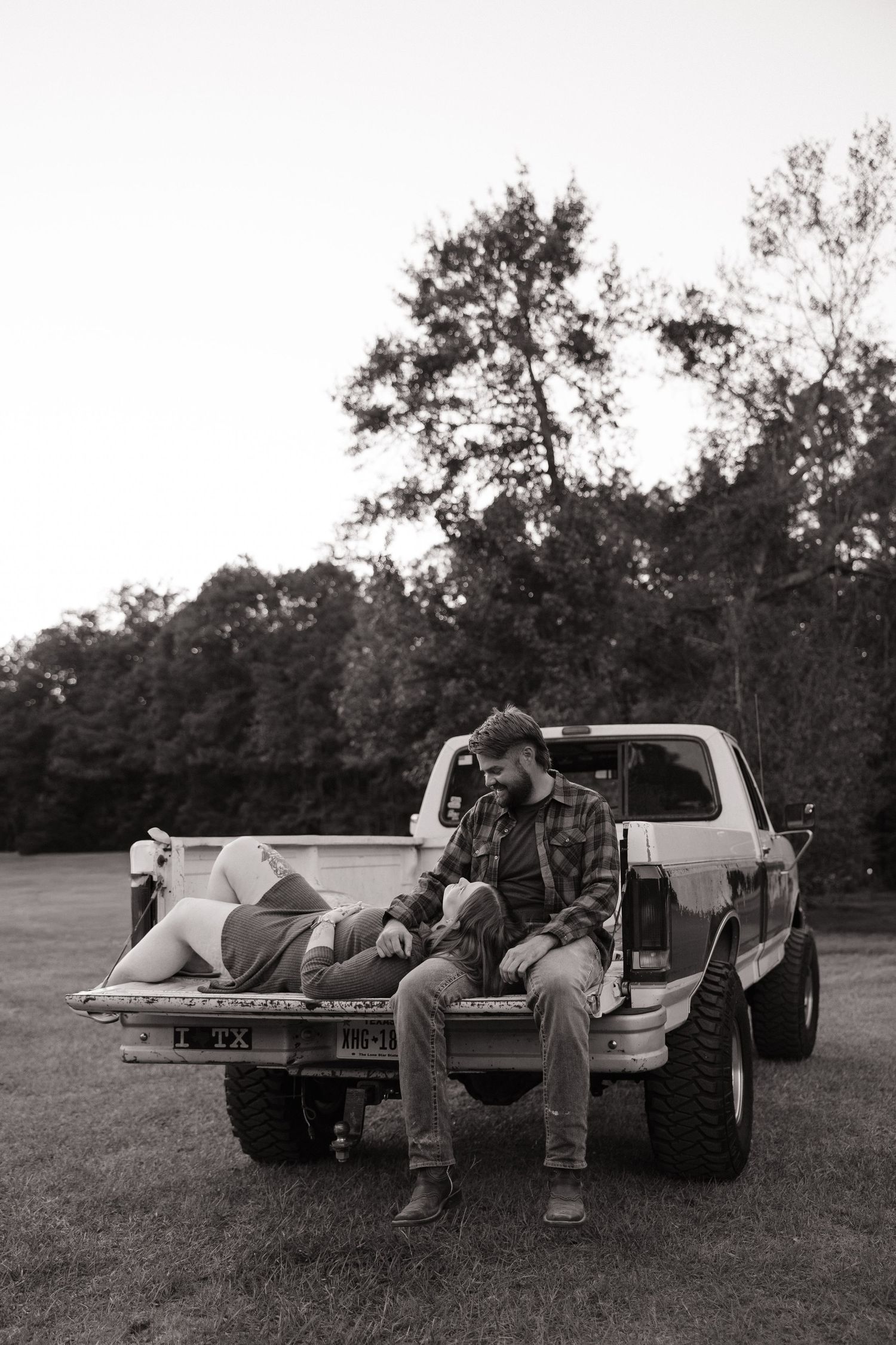 A series of black and white photos showing people relaxing in the back of a pickup truck in a grassy field.