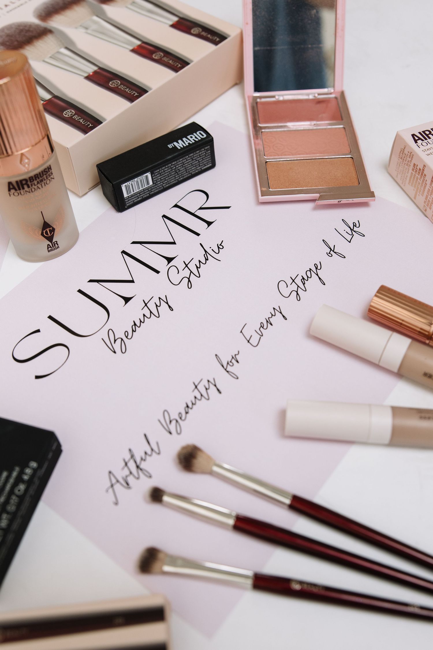 Flatlay of luxury makeup products including brushes and cosmetics with text 'SULAIR' written on pink paper.