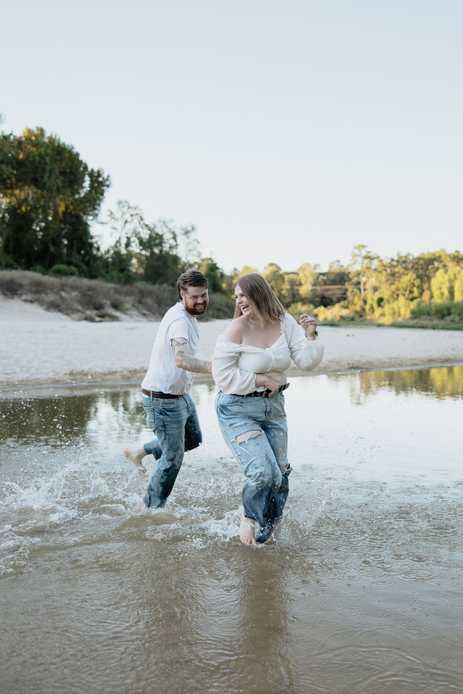 A couple plays and splashes in shallow water at the beach during sunset, creating joyful moments together.