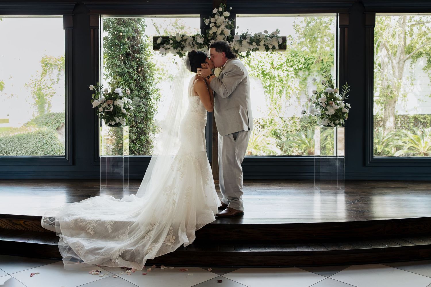 Romantic moment captured in front of large windows during wedding ceremony.