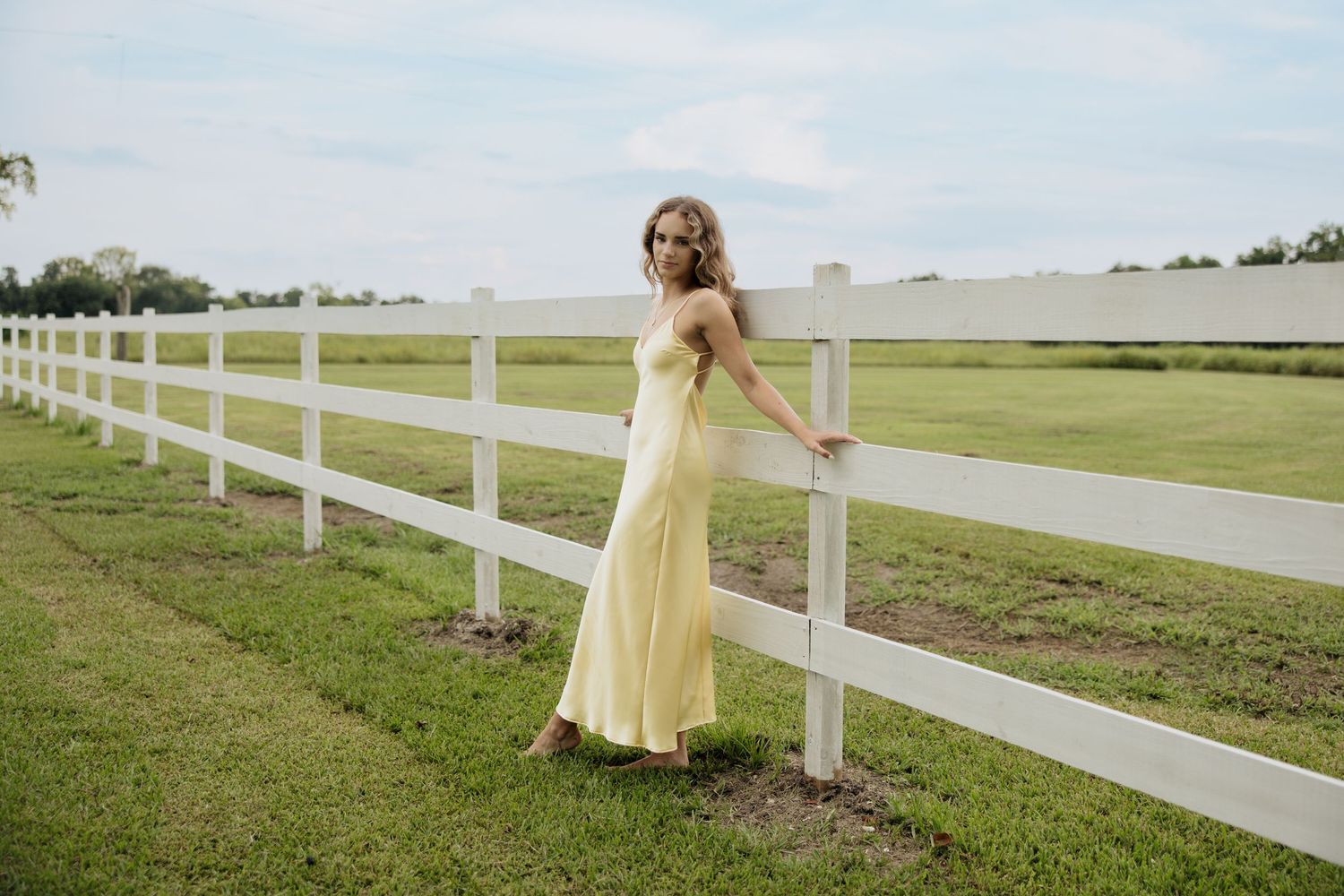 Pastoral scene with white fence stretching along a grassy field on a sunny day.