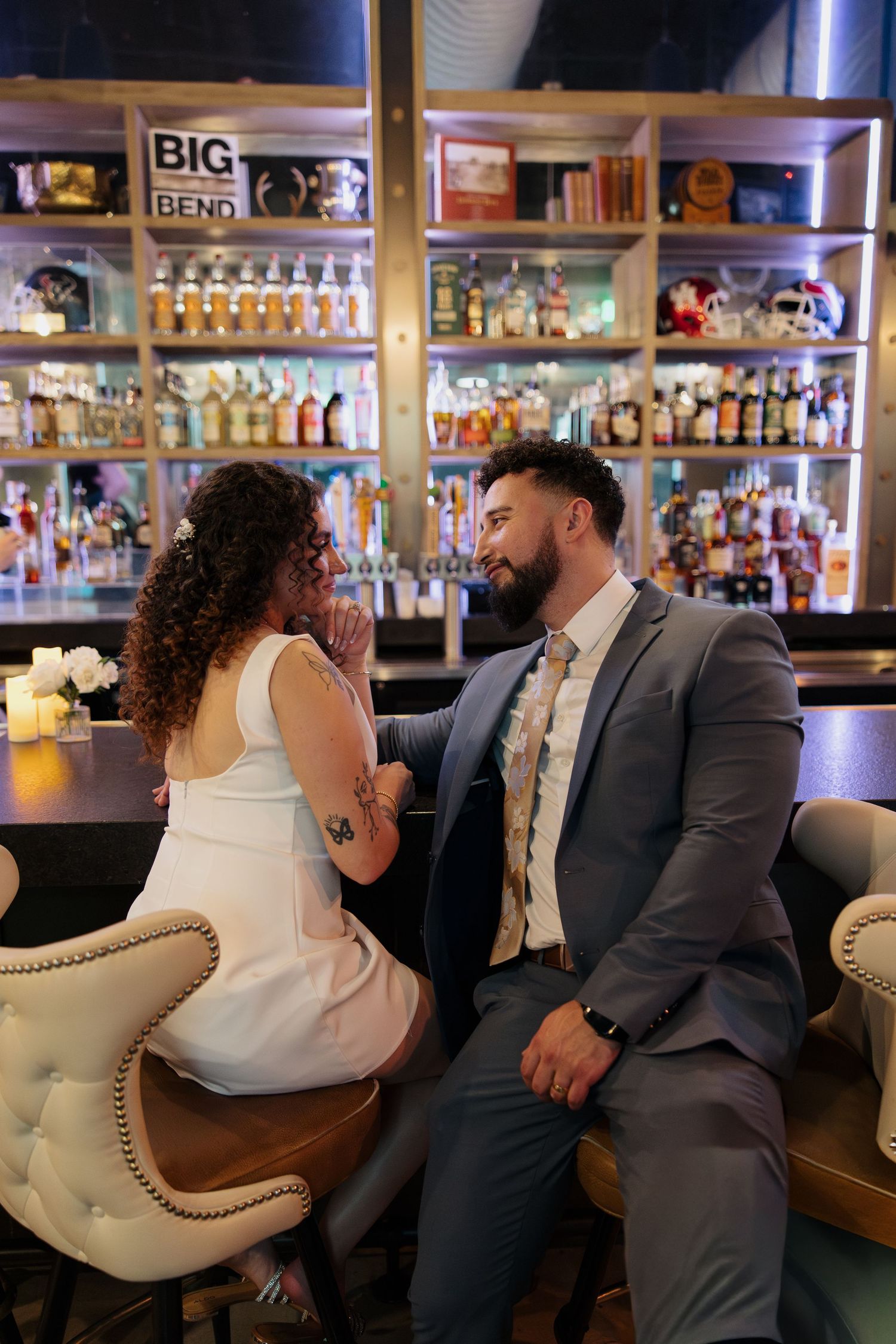 Couple sharing tender moments while seated on an elegant tufted bench in a bar setting.