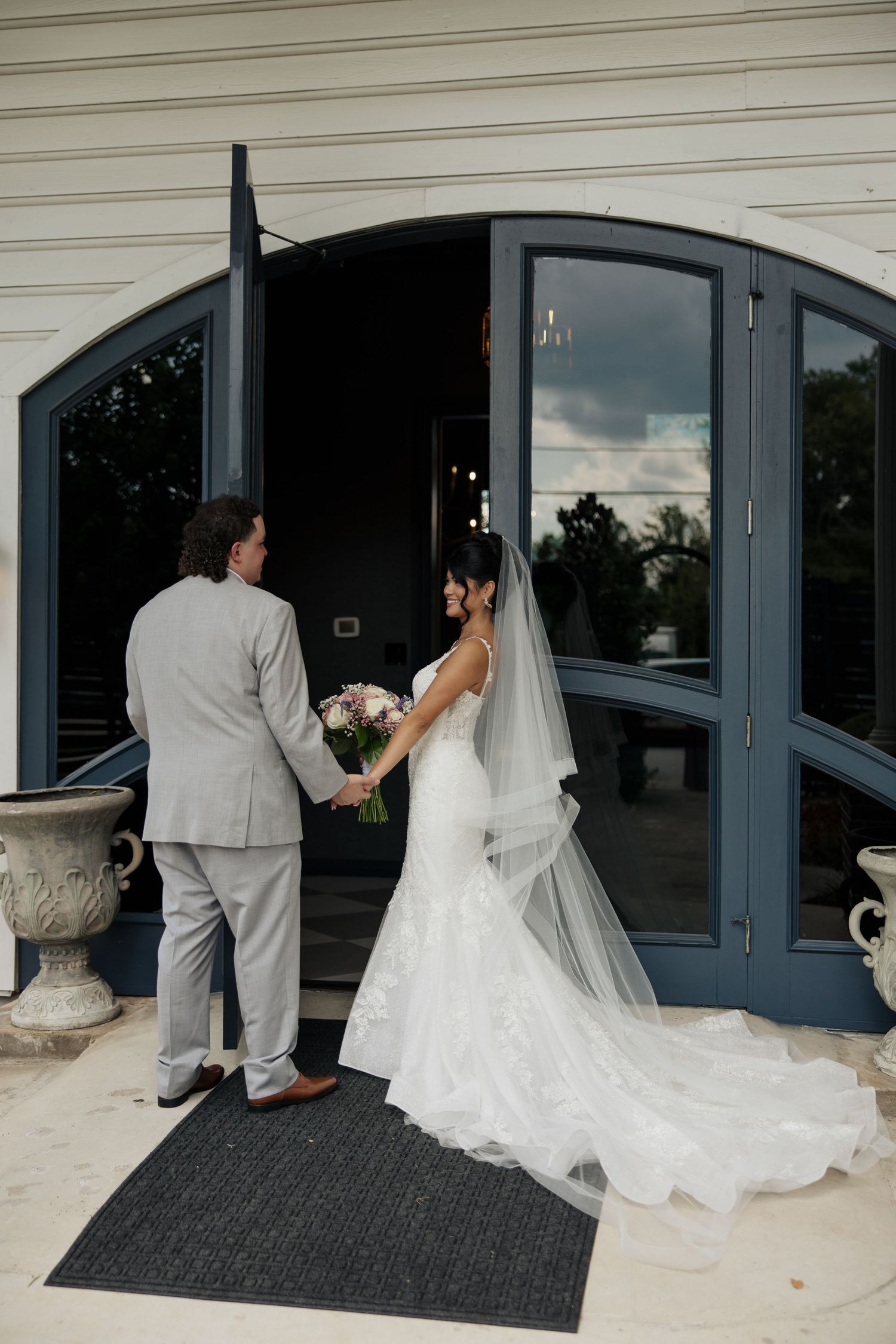 Wedding couple entering building through modern glass doors with flowing white dress.