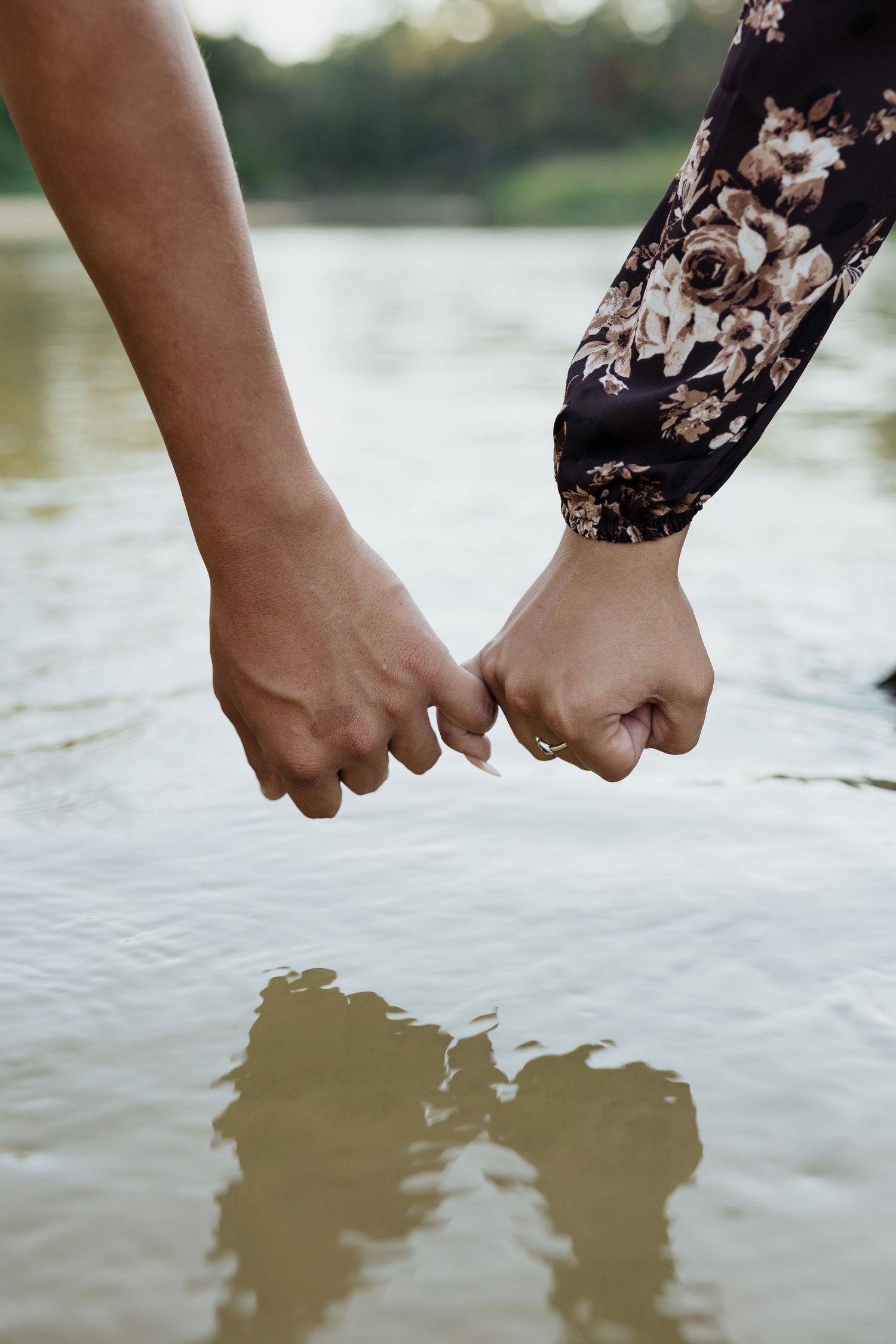 Close-up of hands reaching down to touch the surface of a calm lake creating ripples in the water.