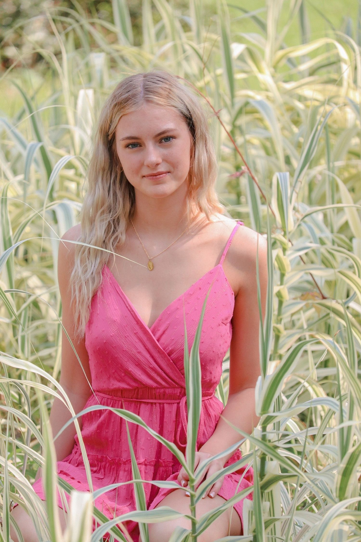 Summer portrait in pink dress among tall grass and natural sunlight.