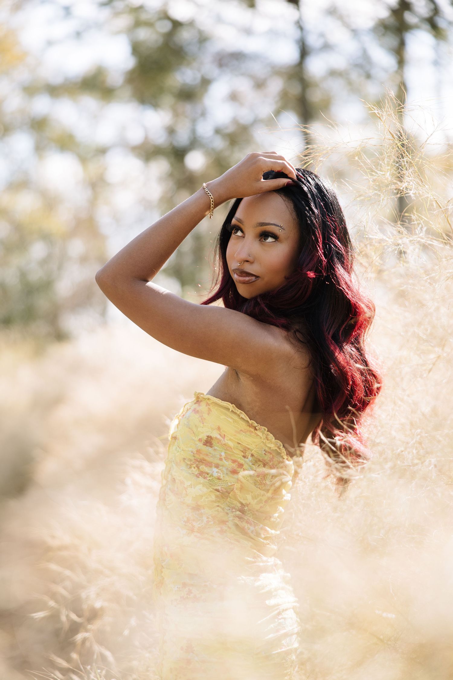 A person in a yellow dress poses gracefully in a sunlit field with golden grass and dreamy bokeh effects.