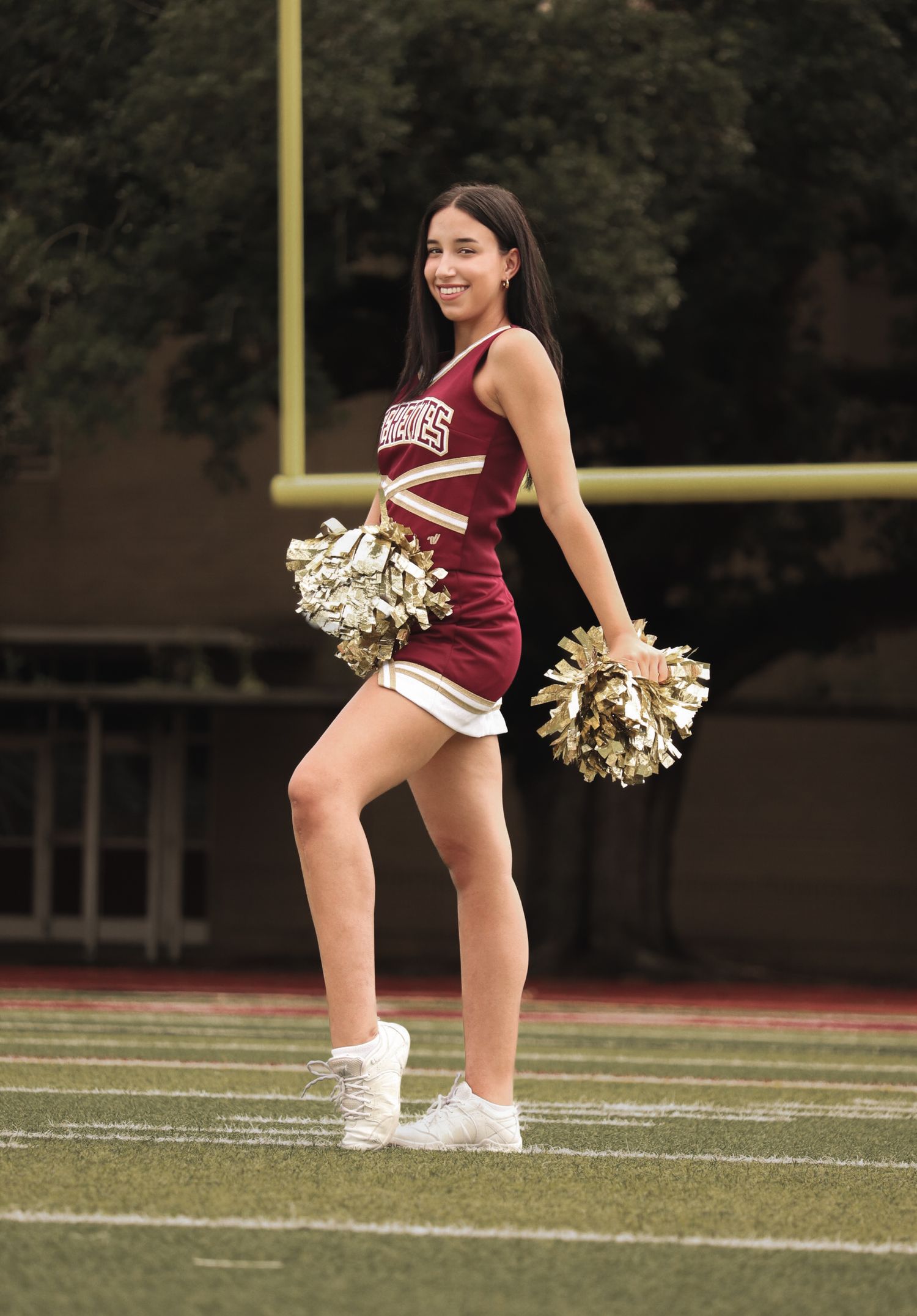 Cheerleader in maroon uniform performs routine on football field.