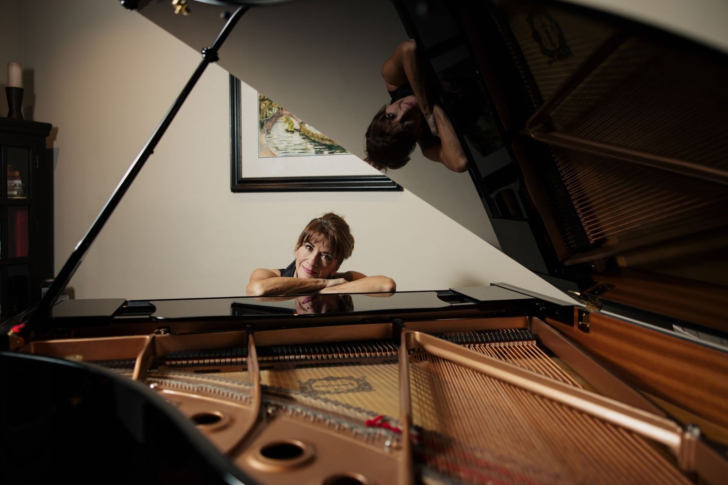 Hands playing a grand piano keyboard in a dimly lit room with sheet music visible in the background.