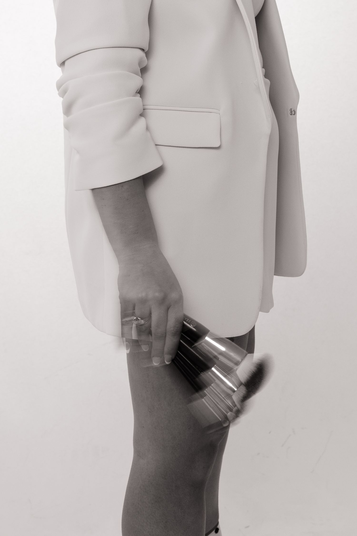 A person in a light gray blazer shown from the side against a white background in a minimalist fashion photograph.