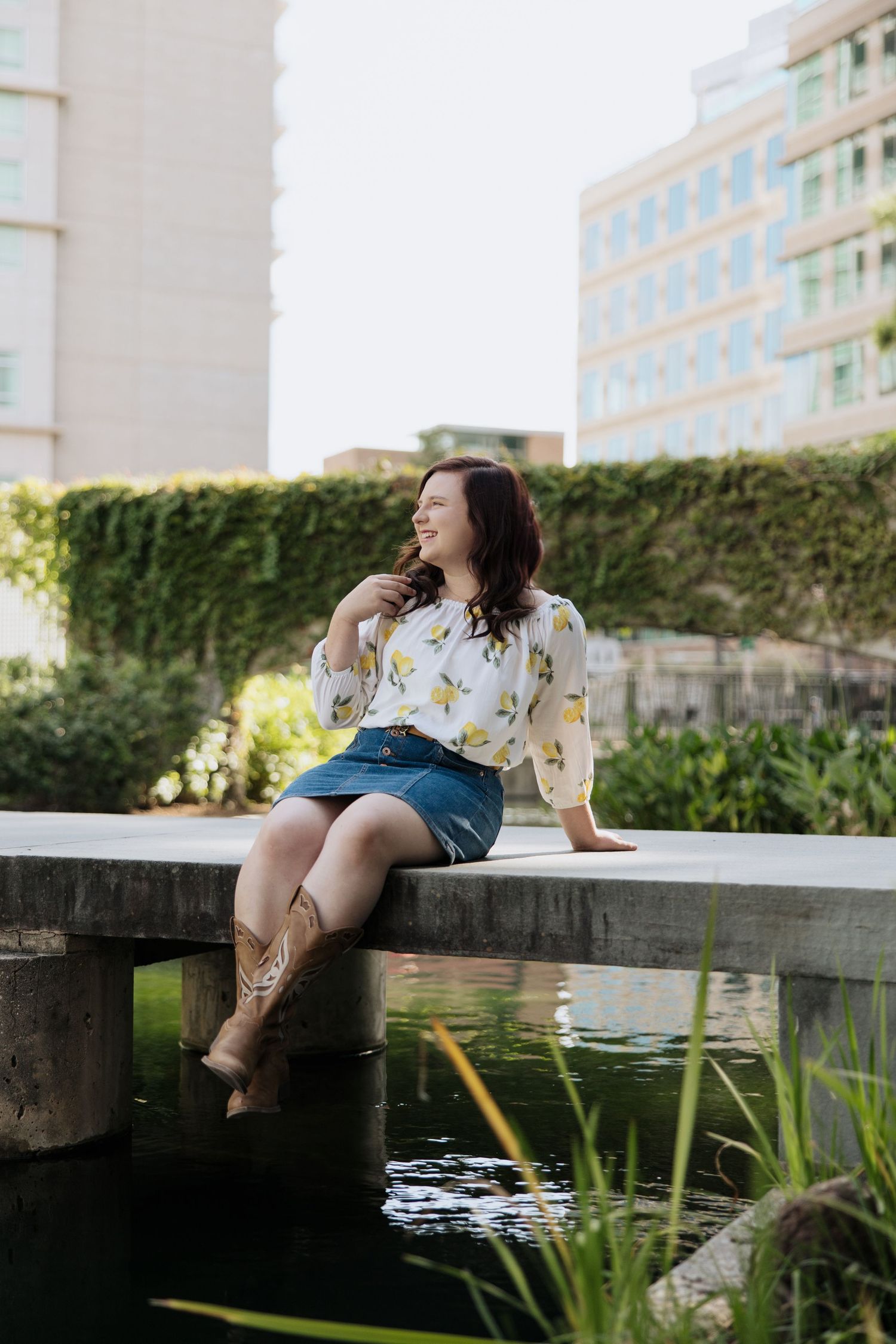 Relaxed summer scene by a pond with water plants and urban architecture in background.