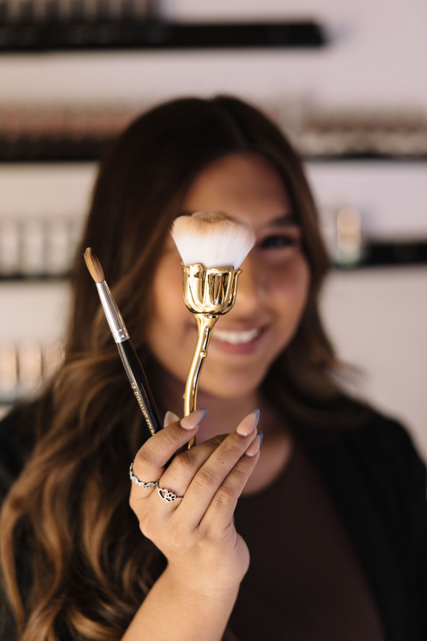 Professional holding a golden makeup brush and smiling in a beauty studio setting.