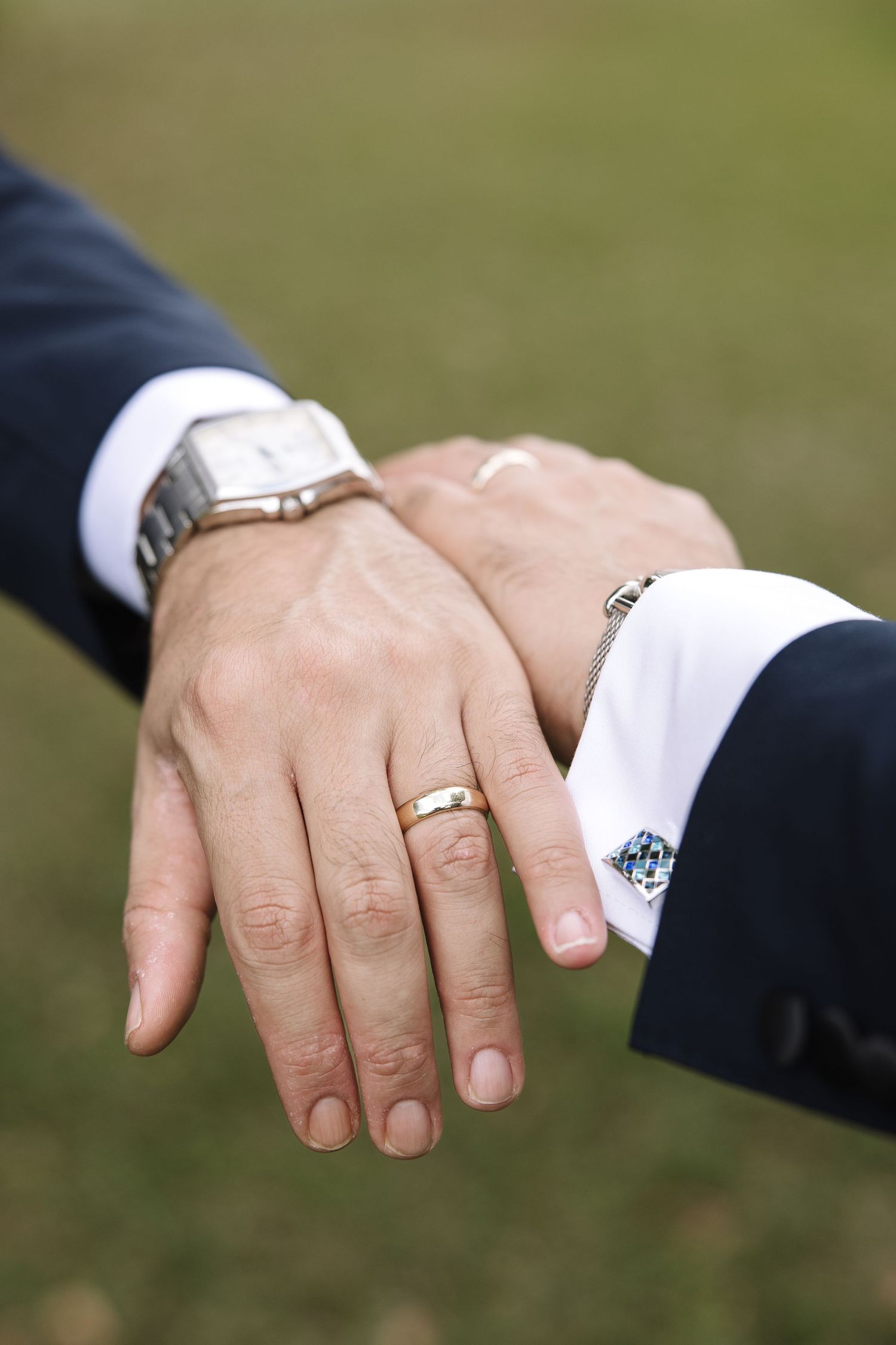 Close-up sequence showing two hands with wedding rings coming together in a romantic gesture against a blurred green background.