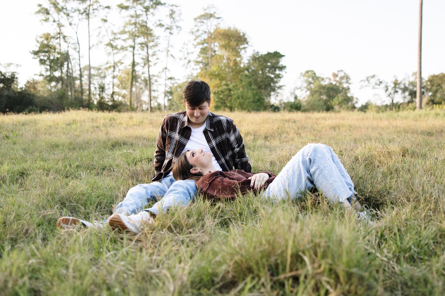 A couple relaxes together on a grassy hillside during a sunny afternoon outdoors.
