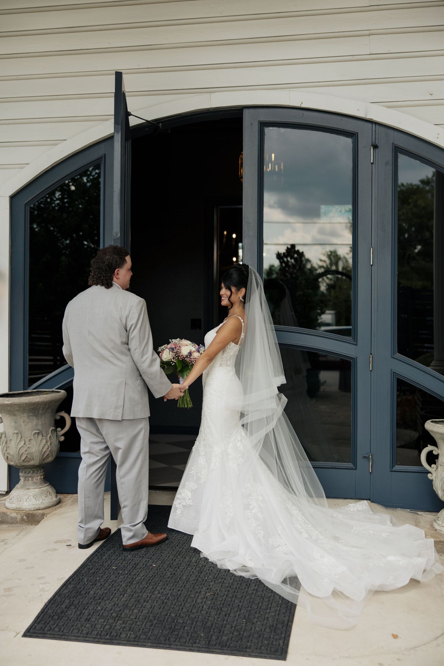 Wedding couple enters through curved glass doors with flowing white wedding dress train.
