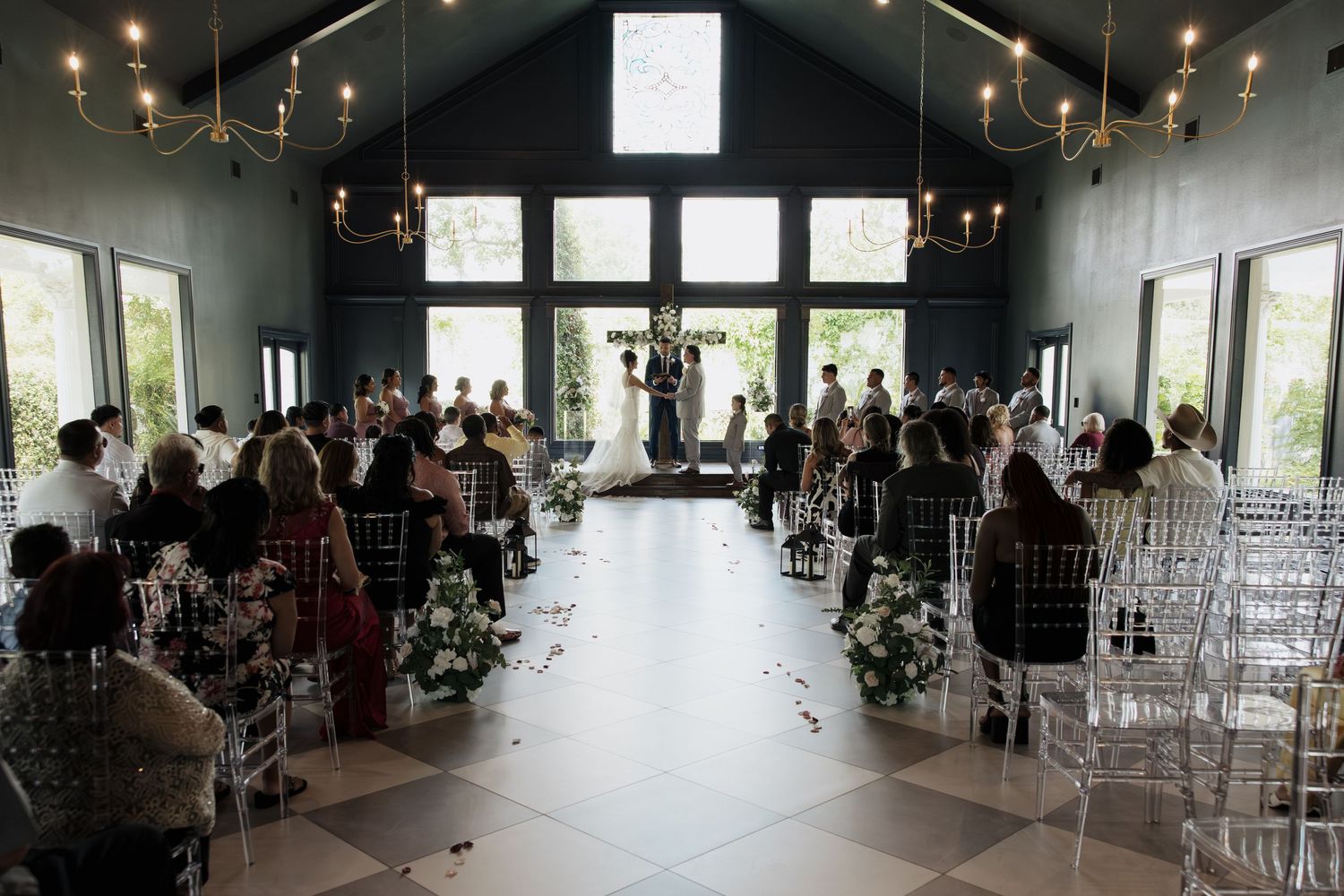 Wedding ceremony in a modern chapel with vaulted ceilings and clear ghost chairs.