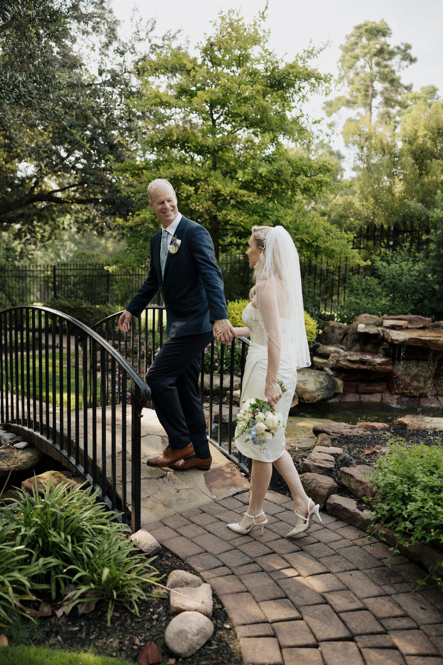 Couple ascends stone garden steps with black iron railing during wedding photoshoot.